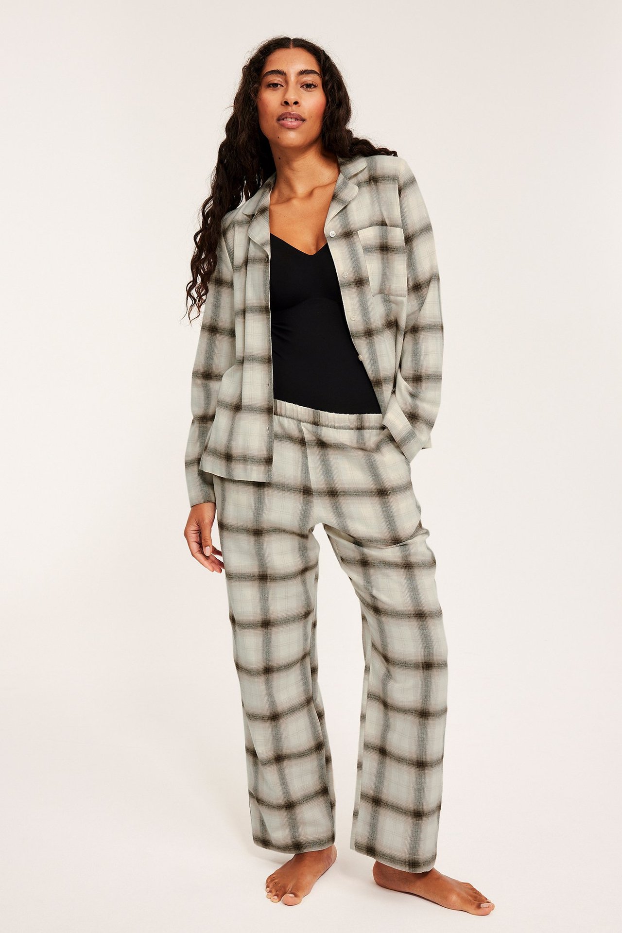 Nainen vaaleabeigeisessä ruudullisessa flanelliyöasutakissa, rento asento.