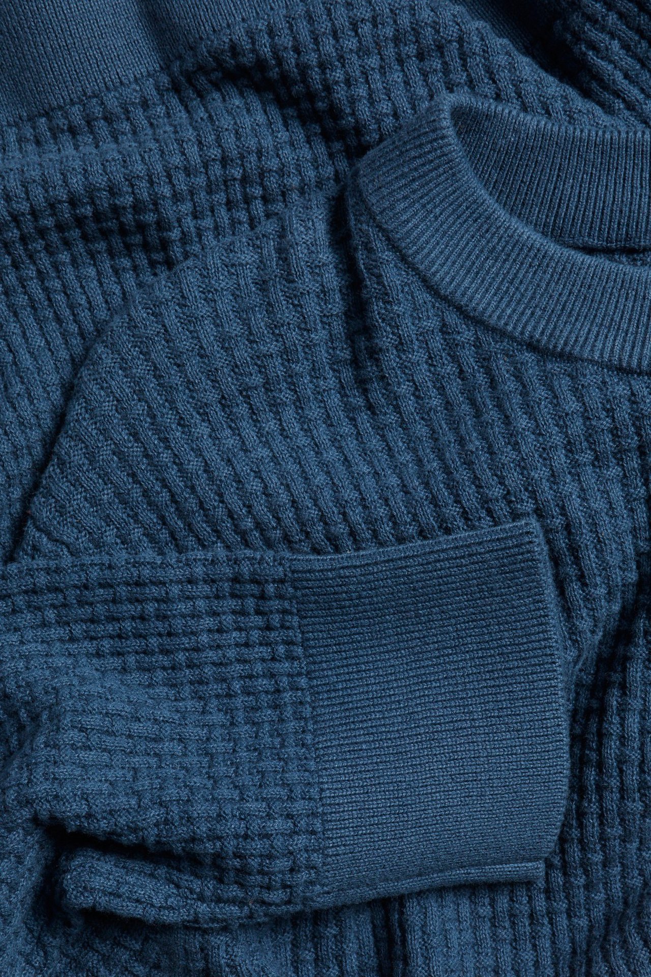 Zbliżenie niebieskiego bawełnianego swetra z dzianiny o teksturowanym wzorze i okrągłym dekolcie.