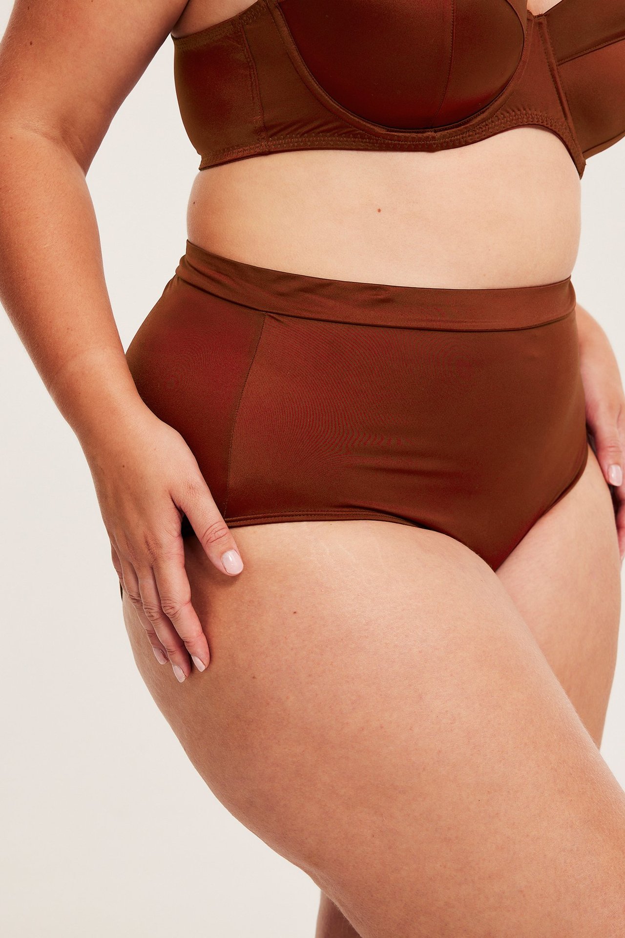 Frontvy av kvinna i högmidjade, glansiga rostfärgade maxitrosor och matchande behå.