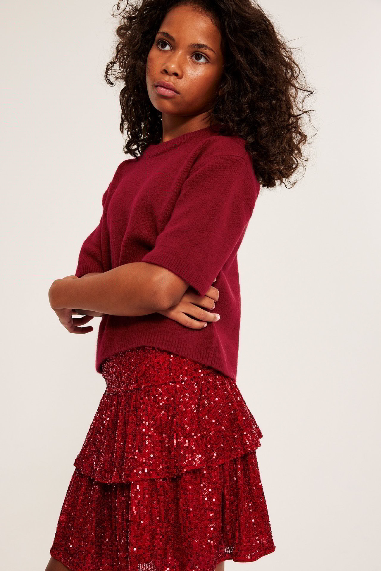 Sidovy av ett barn i en röd finstickad kortärmad tröja och en röd paljettkjol.