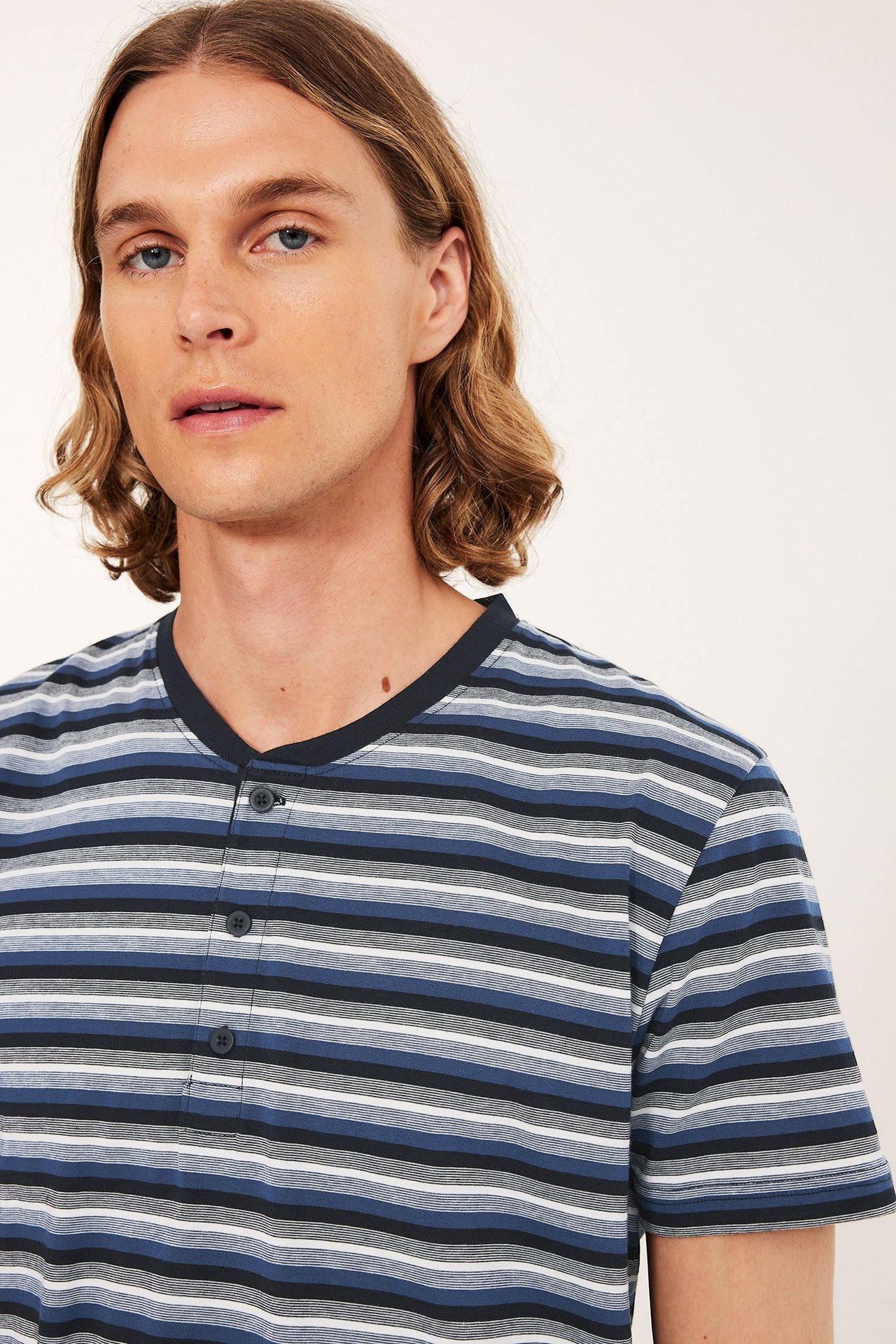 Edestä näkymä miehestä raidallisessa puuvillapyjamapaidassa, jossa sinisiä, harmaita, valkoisia, mustia raitoja, henley-kaulus.