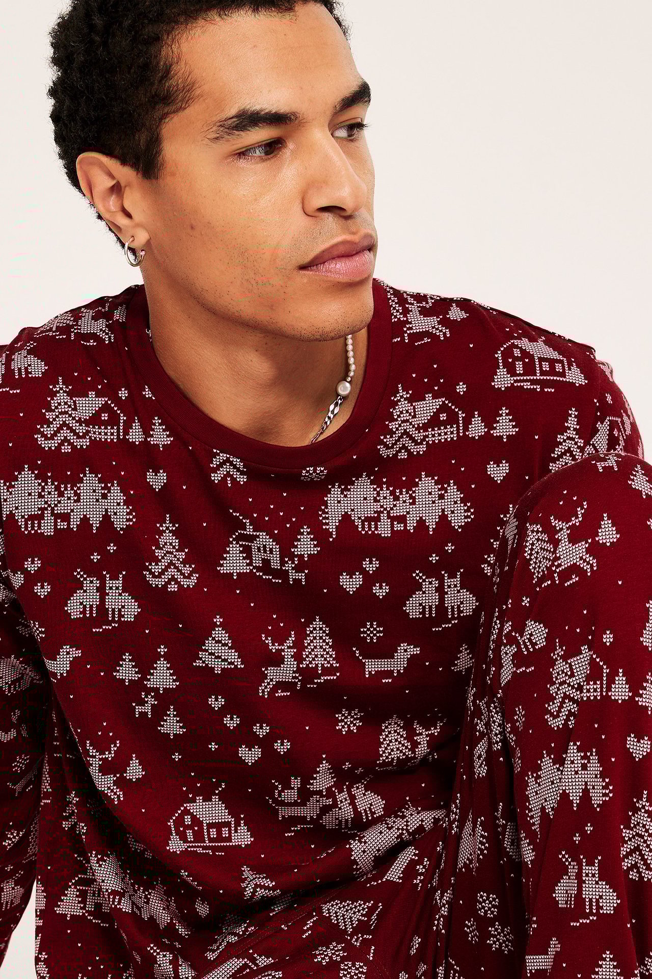 Människa i julpyjamas i mörkröd med julmotiv och mudd på topp och byxa.