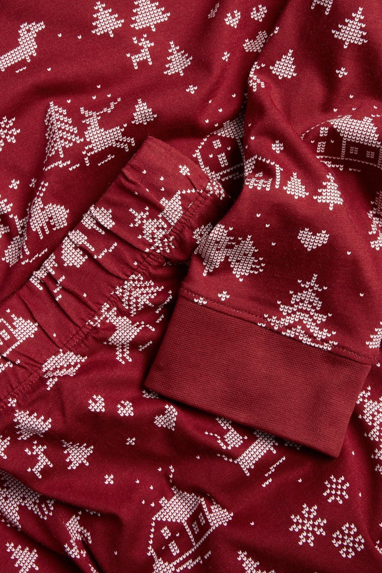 Zbliżenie na ciemnoczerwoną piżamę bawełnianą z białym świątecznym wzorem, reniferami i drzewkami, oraz ściągaczami.