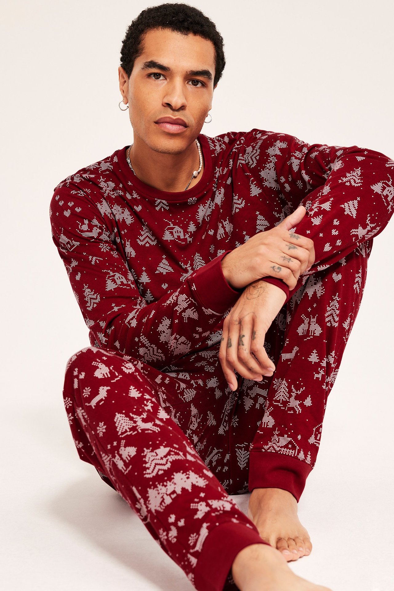Mann i mørkerød julepyjamas med mønster, rund hals, manchetter på topp og bukse.