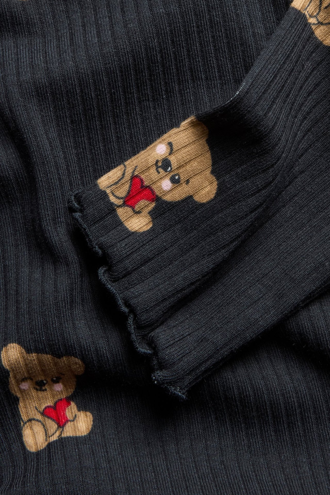 Zbliżenie na czarny, prążkowany top z długim rękawem we wzór brązowych misiów trzymających czerwone serca.