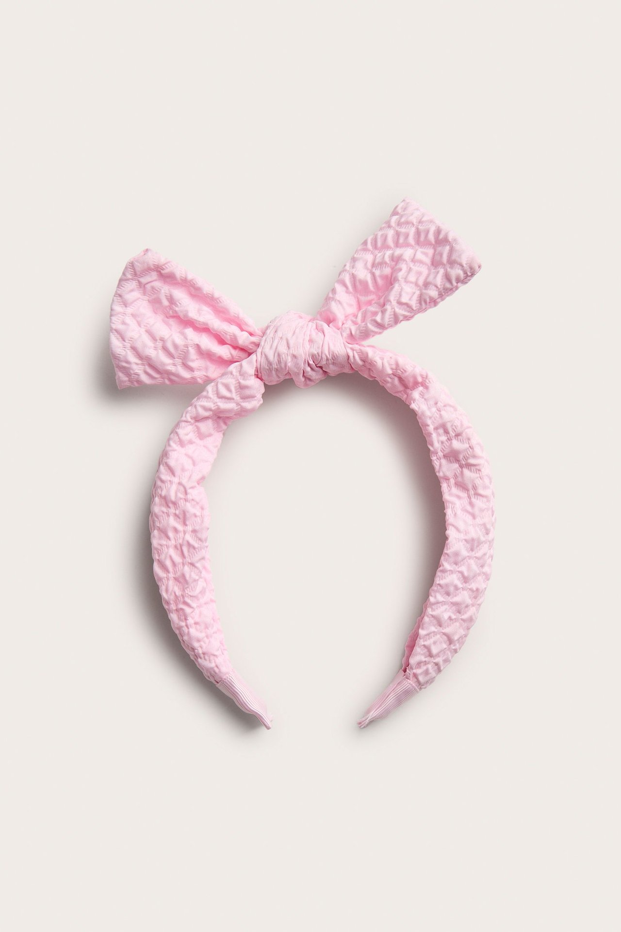 Widok z przodu jasnoróżowej teksturowanej opaski do włosów z kokardą zawiązaną u góry.