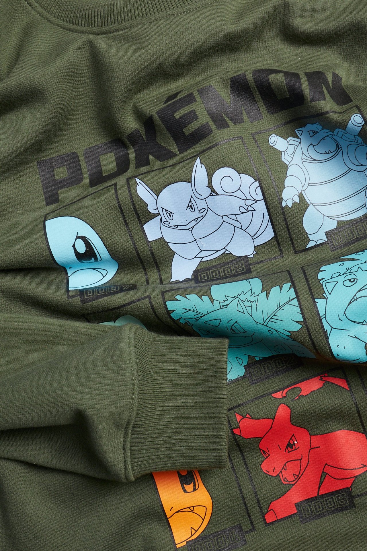 Zbliżenie, przód: ciemnozielona bluza dziecięca z tekstem "POKÉMON" i kolorowym nadrukiem postaci.