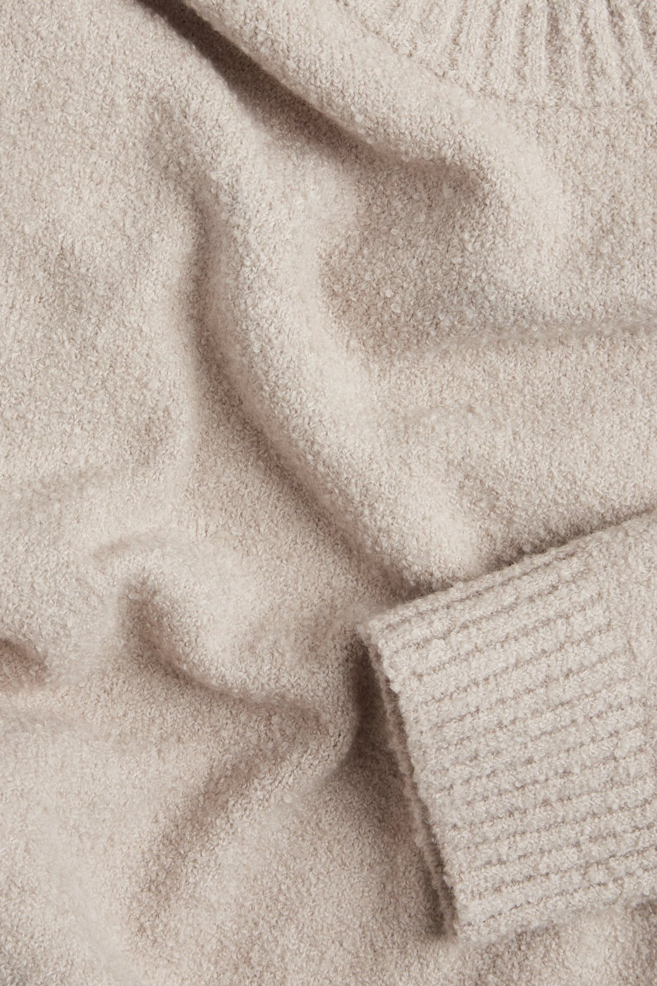 Zbliżenie beżowego swetra z dzianiny boucle z prążkowanym mankietem.