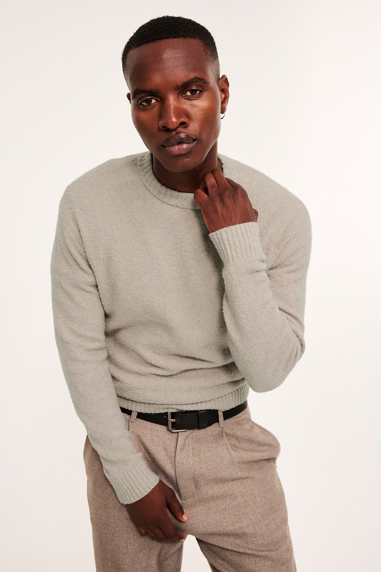 Frontbilde av mann i beige bouclé strikkegenser med rund hals, beige bukse og svart belte.