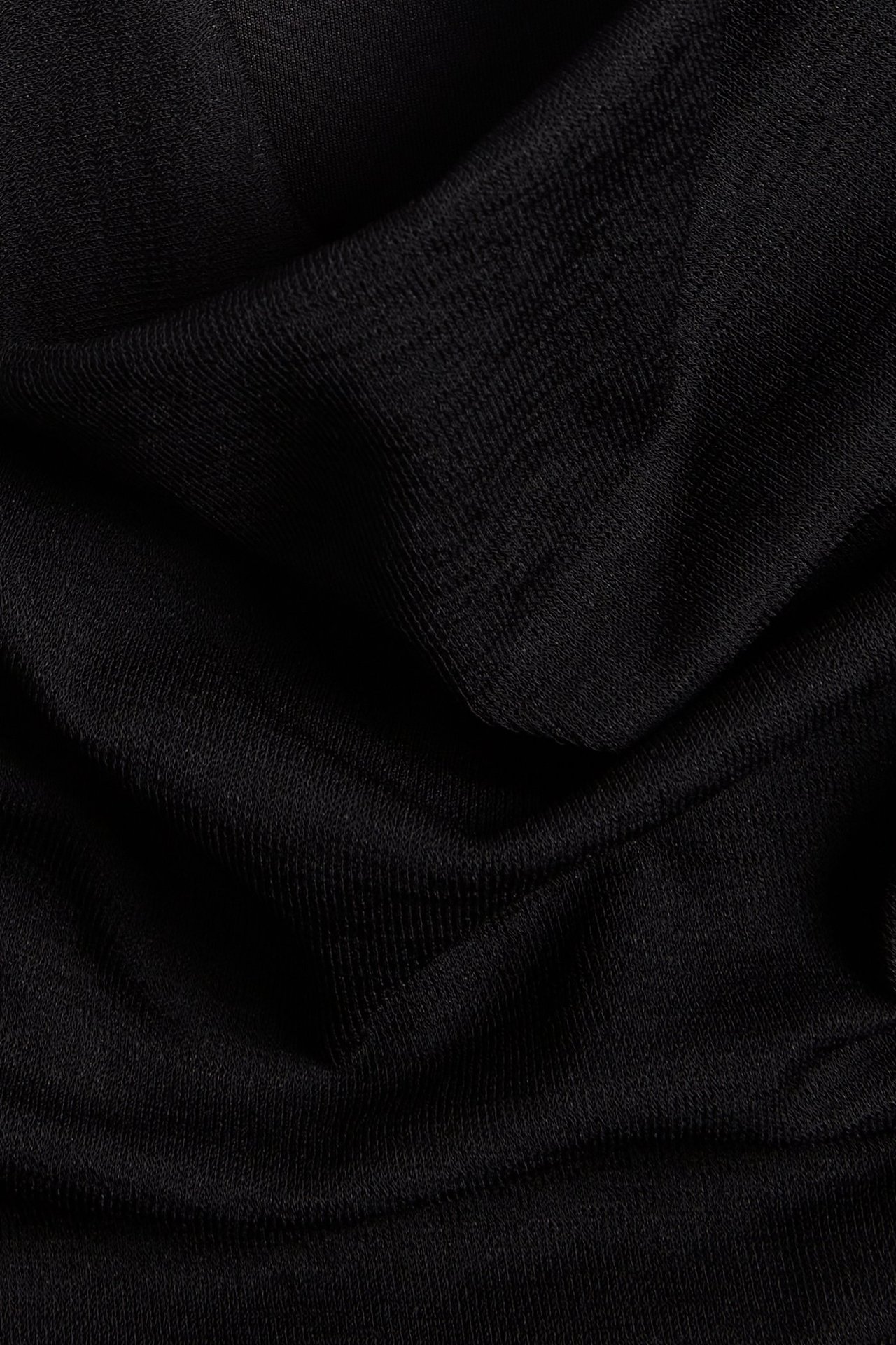 Nærbilde av svart drapert stoff, som viser dets myke, ensfargede tekstur og elegante folder.
