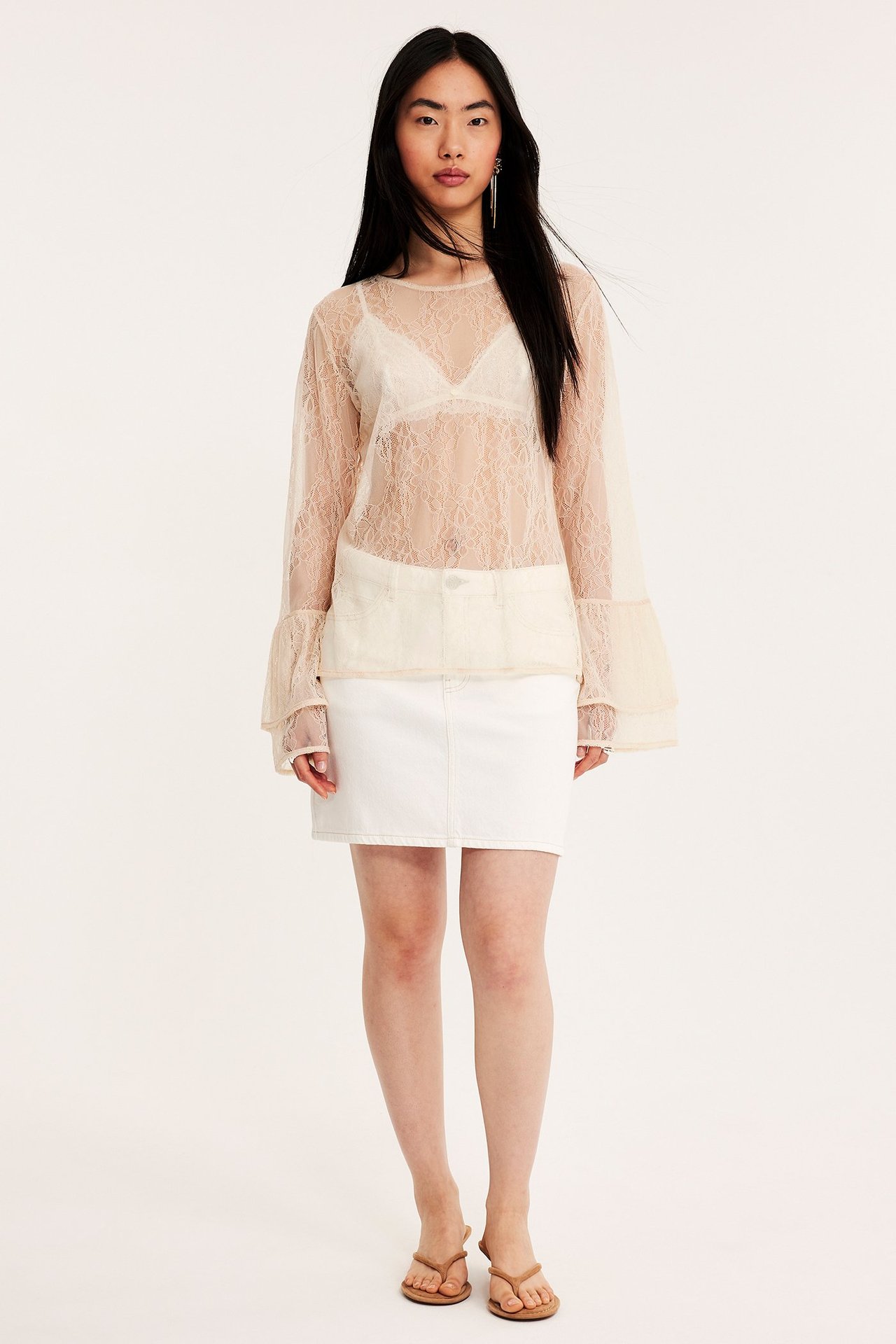 Forfra: kvinne i offwhite blondebluse med puffermer over bralette, hvitt miniskjørt, brune sandaler.