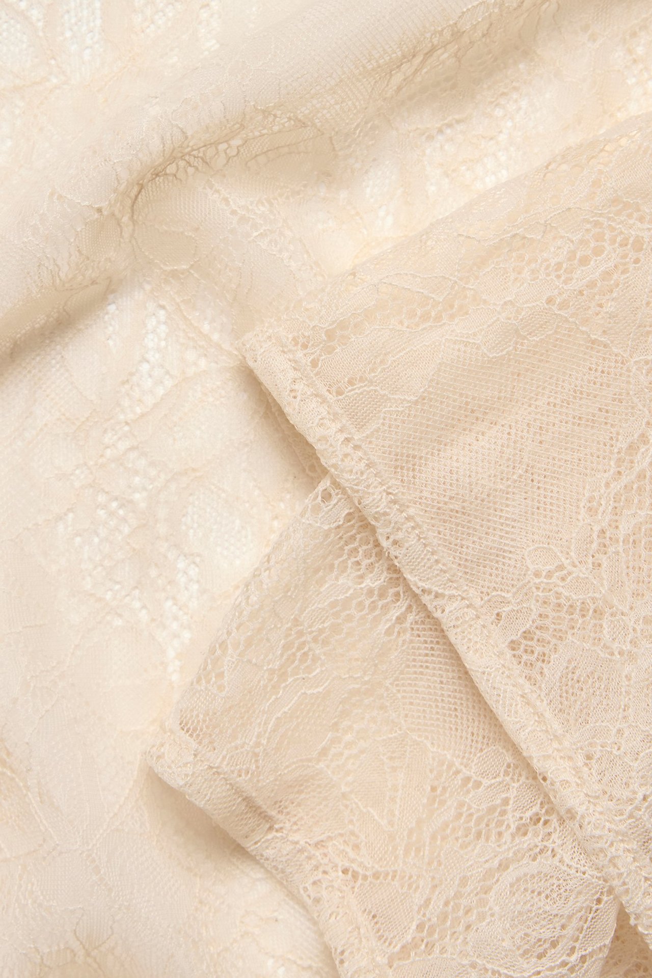 Zbliżenie na ecru koronkową tkaninę bluzki z delikatnym kwiatowym wzorem.