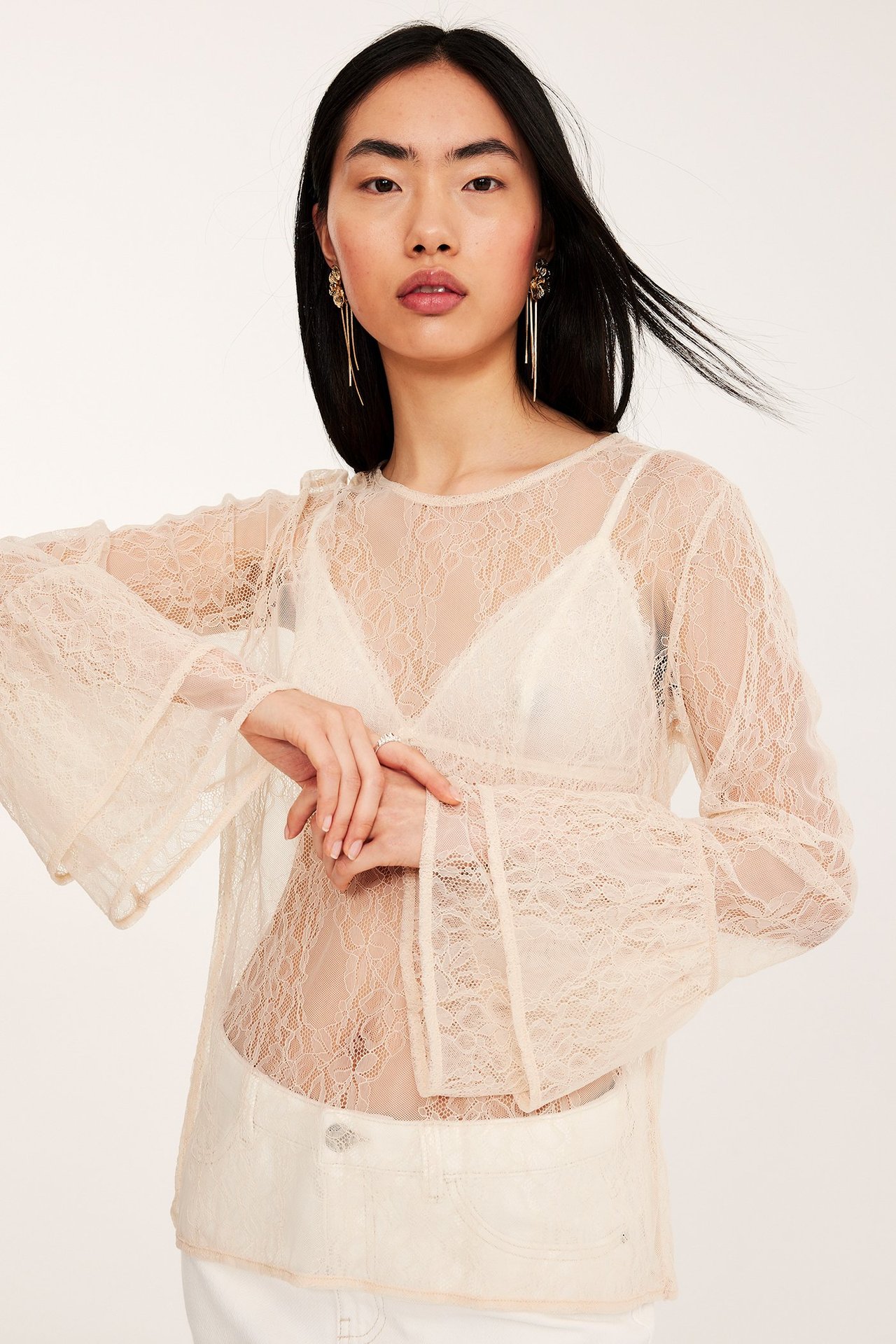 Forfra: kvinne i offwhite gjennomsiktig blondebluse, puffermer, hvit bralette og hvite bukser.