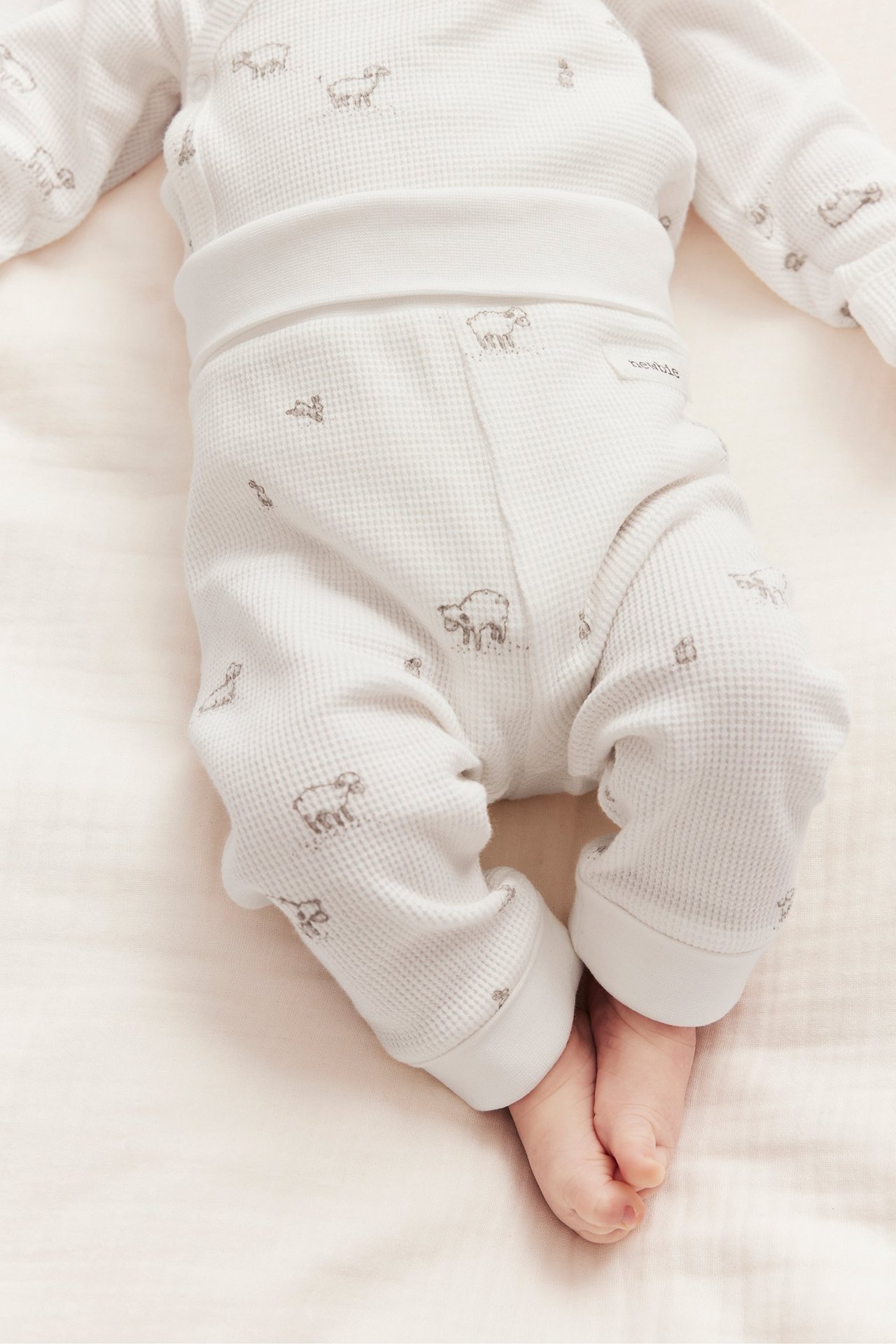 Närbild på baby i offwhite våfflade leggings med lammönster och breda muddar.