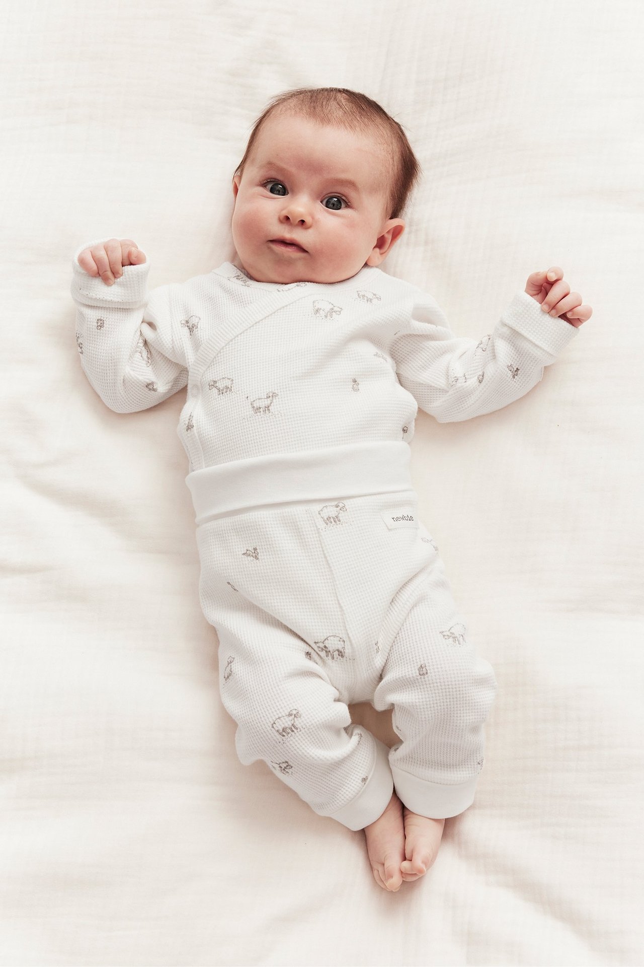 Ovanifrån, baby i offwhite våfflade leggings och matchande omlott-topp med lammönster.