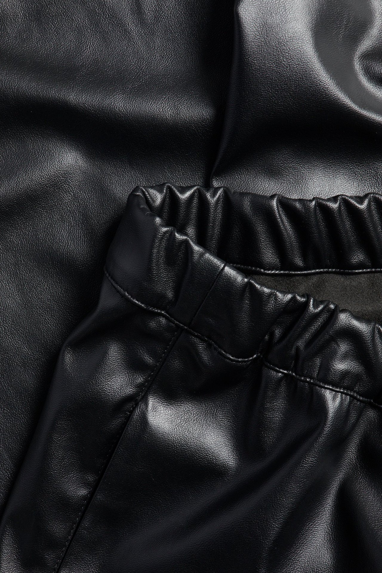 Zbliżenie czarnych spodni pull-on ze sztucznej skóry z elastyczną talią i regulowanym otworem nogawki.