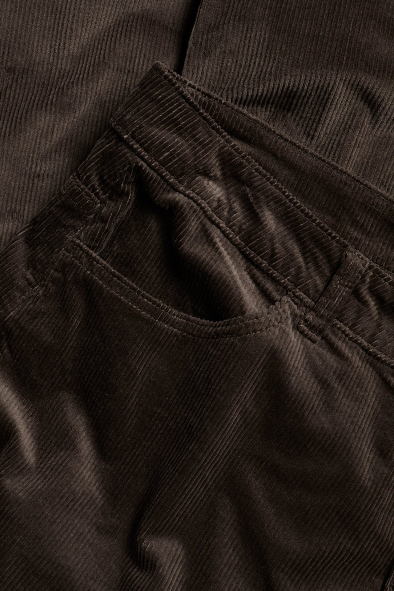Zbliżenie na ciemnobrązowe sztruksowe spodnie, pokazujące przednią kieszeń i pas.