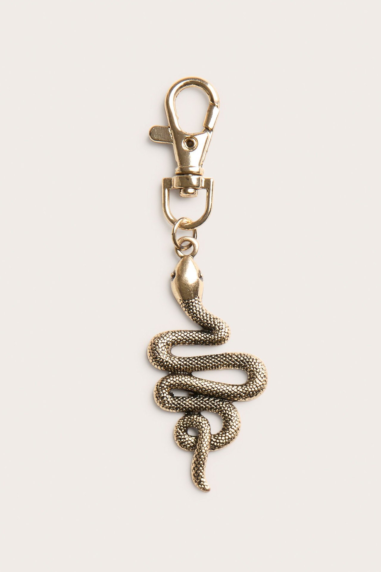 Närbild framifrån av ett guldfärgat ormformat metallhänge med texturerad yta, fäst vid en karbinhake.