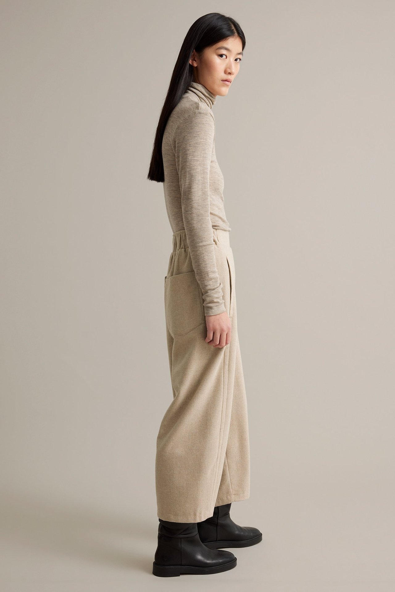 Nainen beige-melange-villasekoitteiset housut sivu- ja takinpuolikkailla, päällä vaalean beige paita.