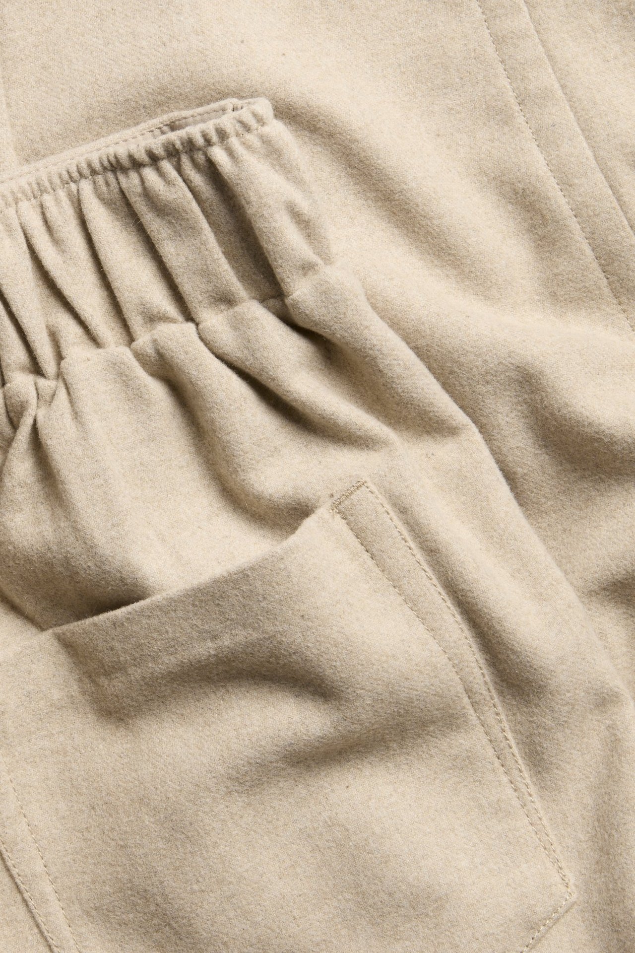 Zbliżenie beżowych spodni z mieszanki wełny z elastycznym pasem i boczną kieszenią.