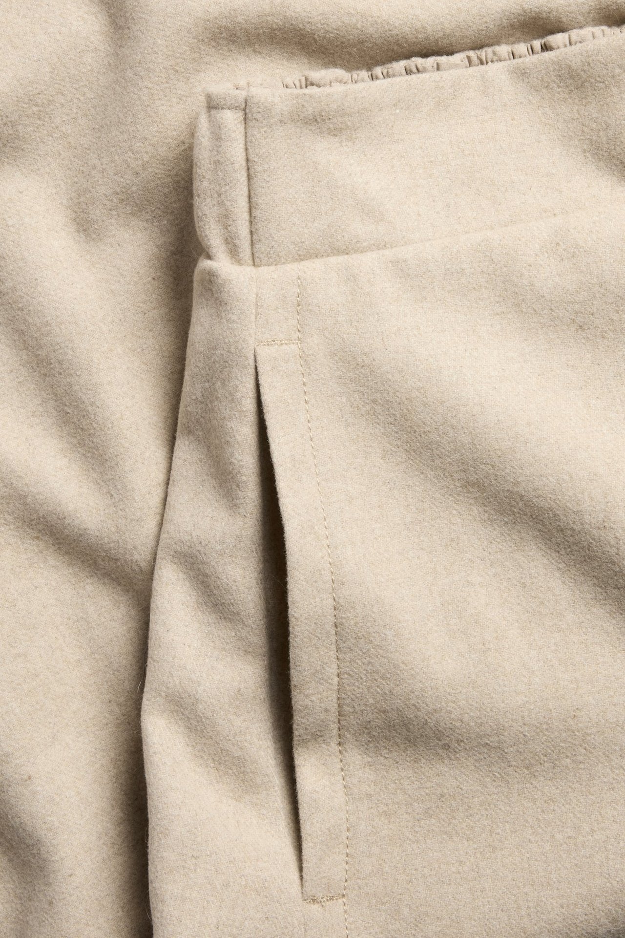 Zbliżenie na beżową, melanżową spódnicę z mieszanki wełny, ukazujące boczną kieszeń.