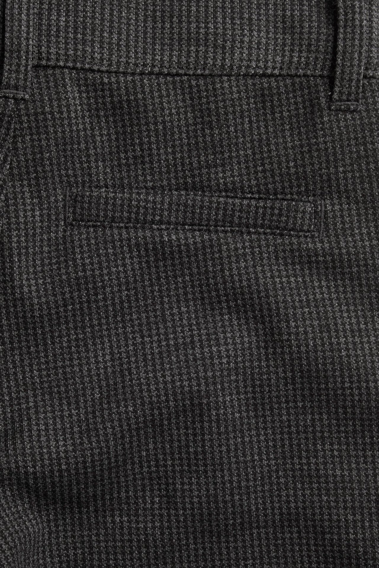 Zbliżenie na dziecięce ciemnoszare wzorzyste spodnie z mieszanki bawełny, z tylną kieszenią i szlufkami.