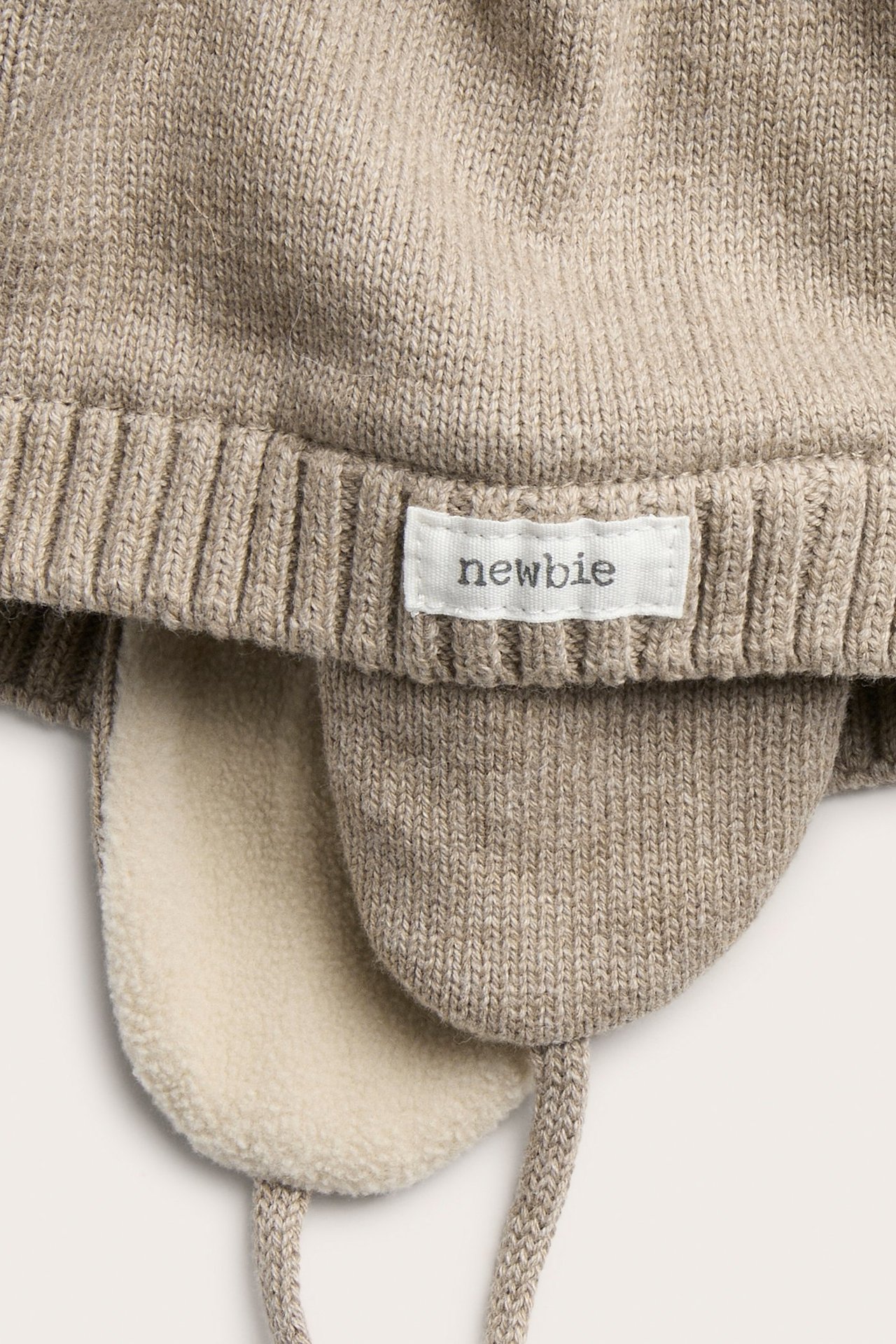 Zbliżenie jasnobrązowej dzianinowej czapki niemowlęcej z nausznikami, wiązaniami i kremową polarową podszewką.
