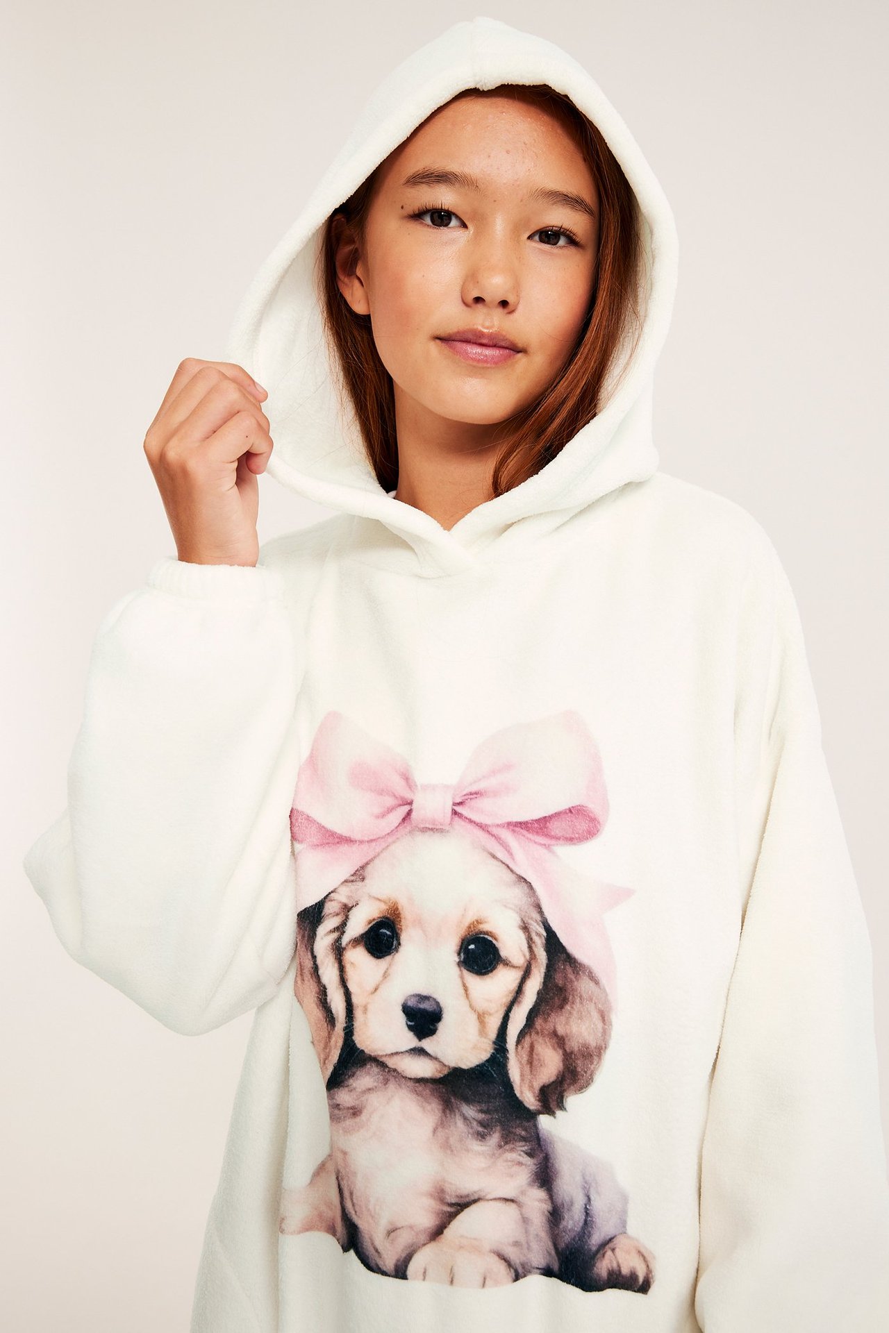 Zbliżenie na dziecko w białym polarowym hoodie z nadrukiem szczeniaka i różowej kokardki z przodu.
