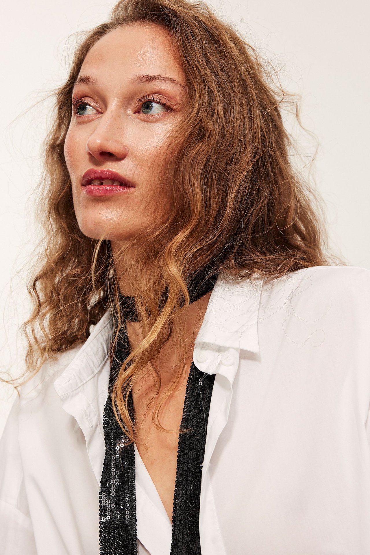 Zbliżenie kobiety w czarnym wąskim poliestrowym szaliku z cekinami na białej koszuli.