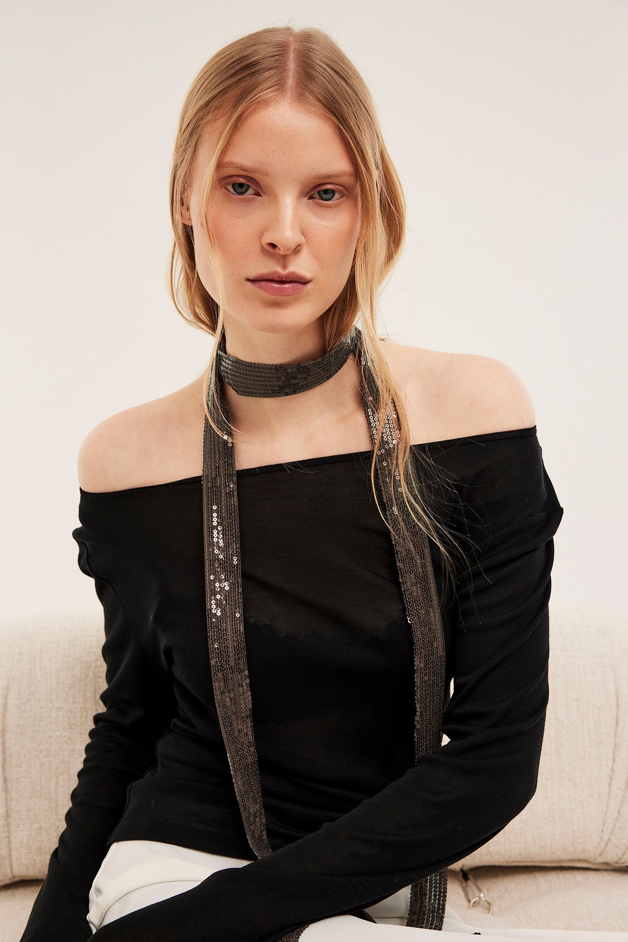 Widok z przodu kobiety w czarnym topie z odkrytymi ramionami, noszącej wąski ciemnobrązowy szalik z siatki z cekinami.