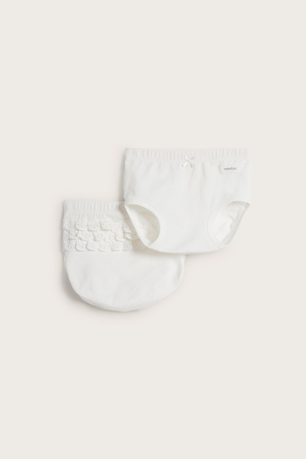 Ovenfra sett to offwhite barneunderbukser, den ene med sløyfe, den andre med blondevolanger.
