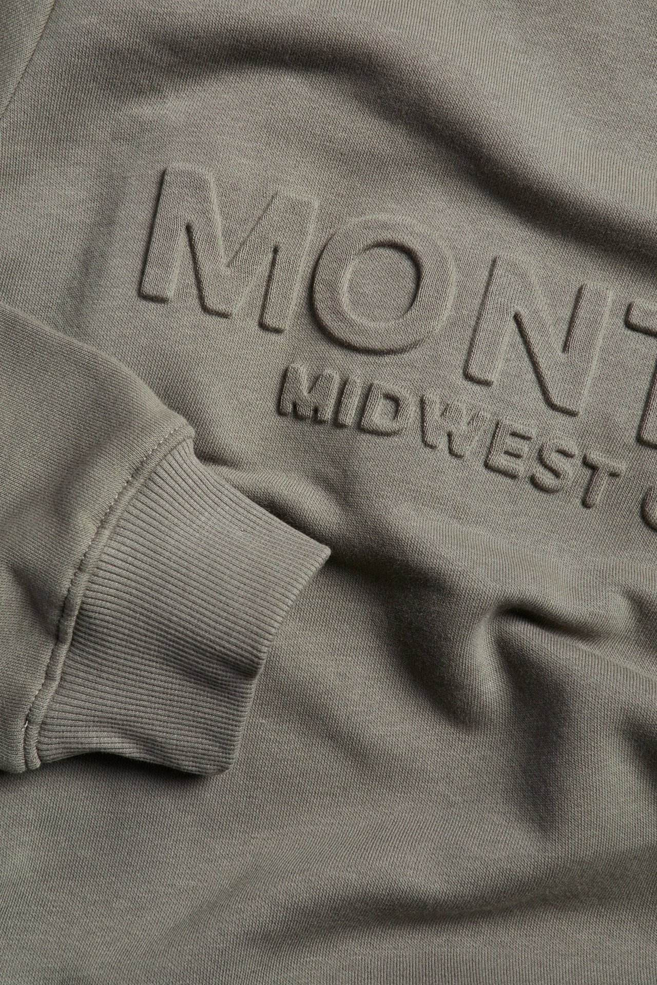 Zbliżenie szarej bluzy z nadrukiem 3D 'MONT MIDWEST' i prążkowanym mankietem.