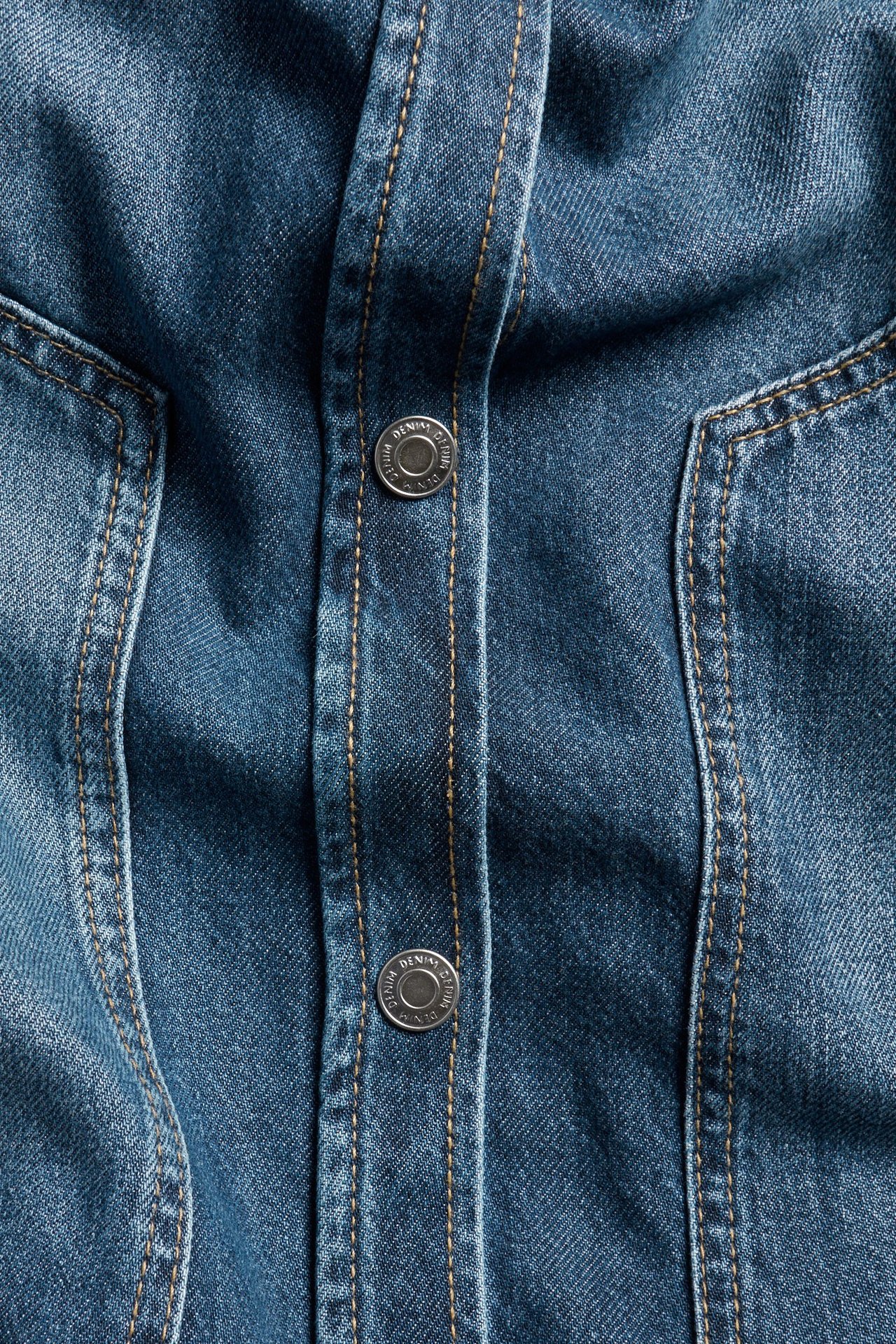 Zbliżenie na niebieską koszulę jeansową ze srebrnymi napami i brązowymi przeszyciami.