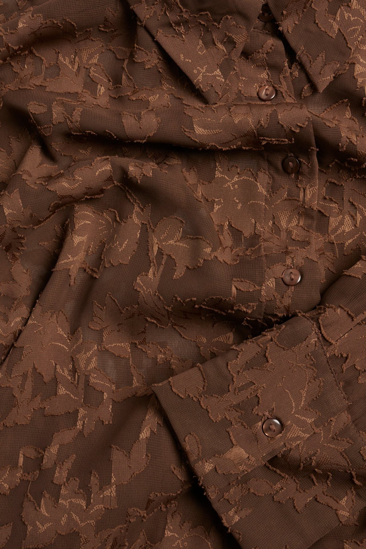 Zbliżenie brązowej koszuli poliestrowej z trójwymiarowym kwiatowym żakardowym wzorem i guzikami.