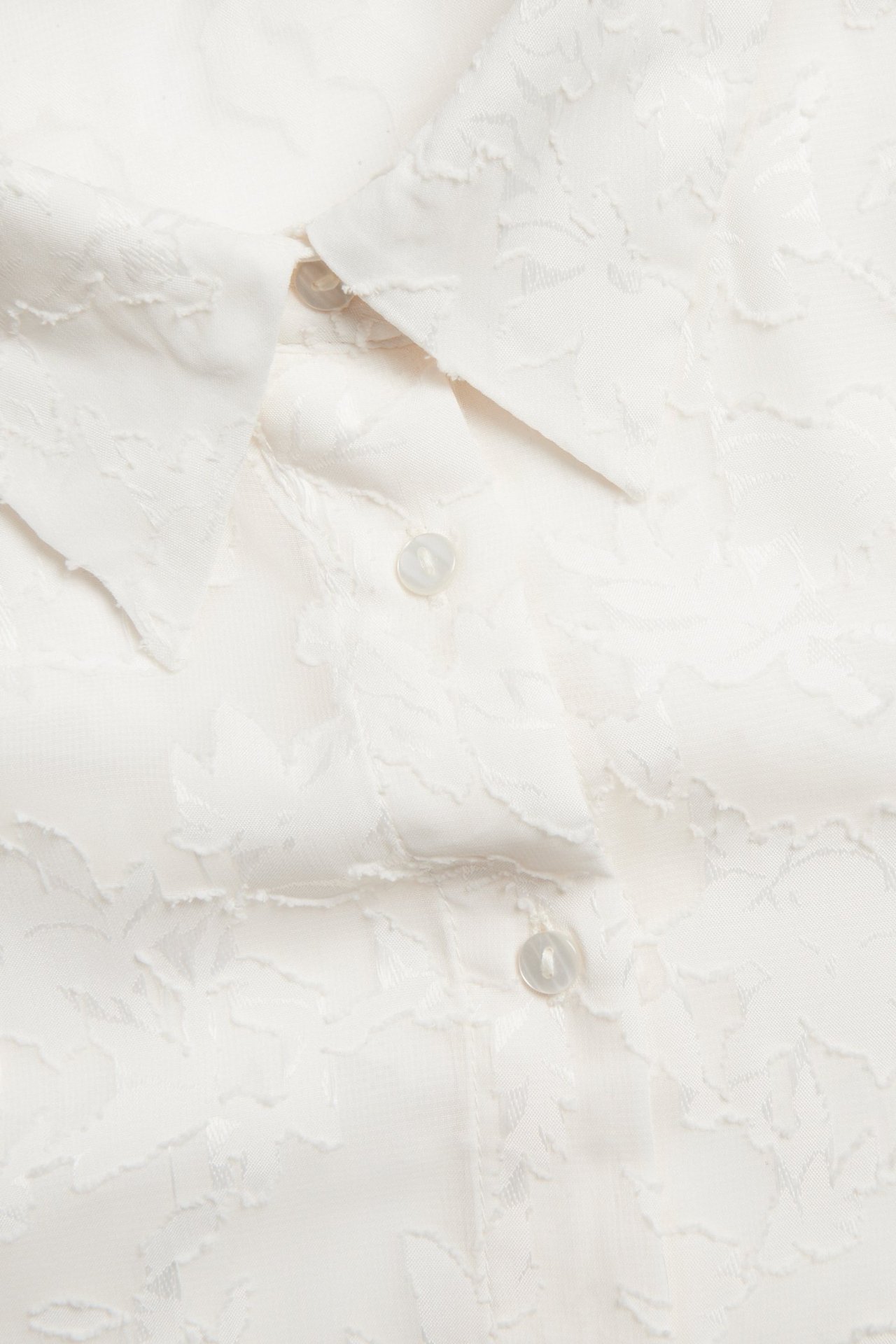 Zbliżenie off-white koszuli damskiej z żakardowym kwiatowym wzorem i przezroczystymi guzikami.