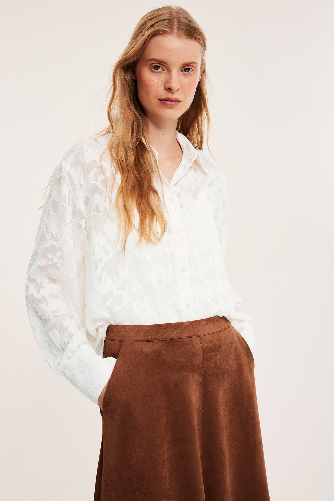 Edestäpäin kuvattu nainen yllään luonnonvalkoinen jacquard-kuvioitu polyesteripaita ja ruskea A-linjainen hame.