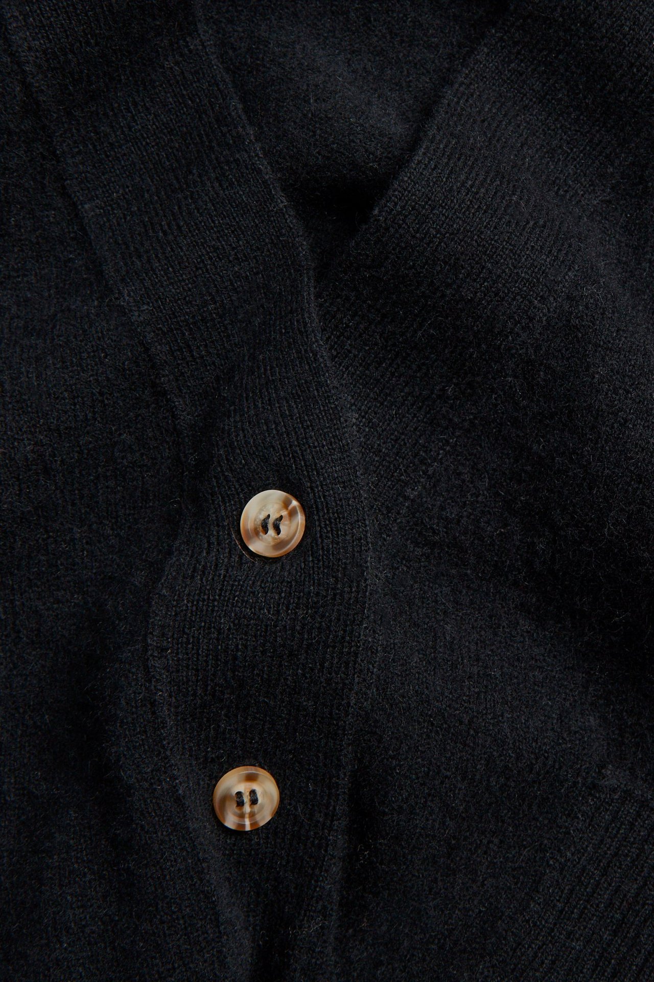 Zbliżenie czarnego kardiganu z mieszanki wełny i kaszmiru z dwoma jasnobrązowymi guzikami.
