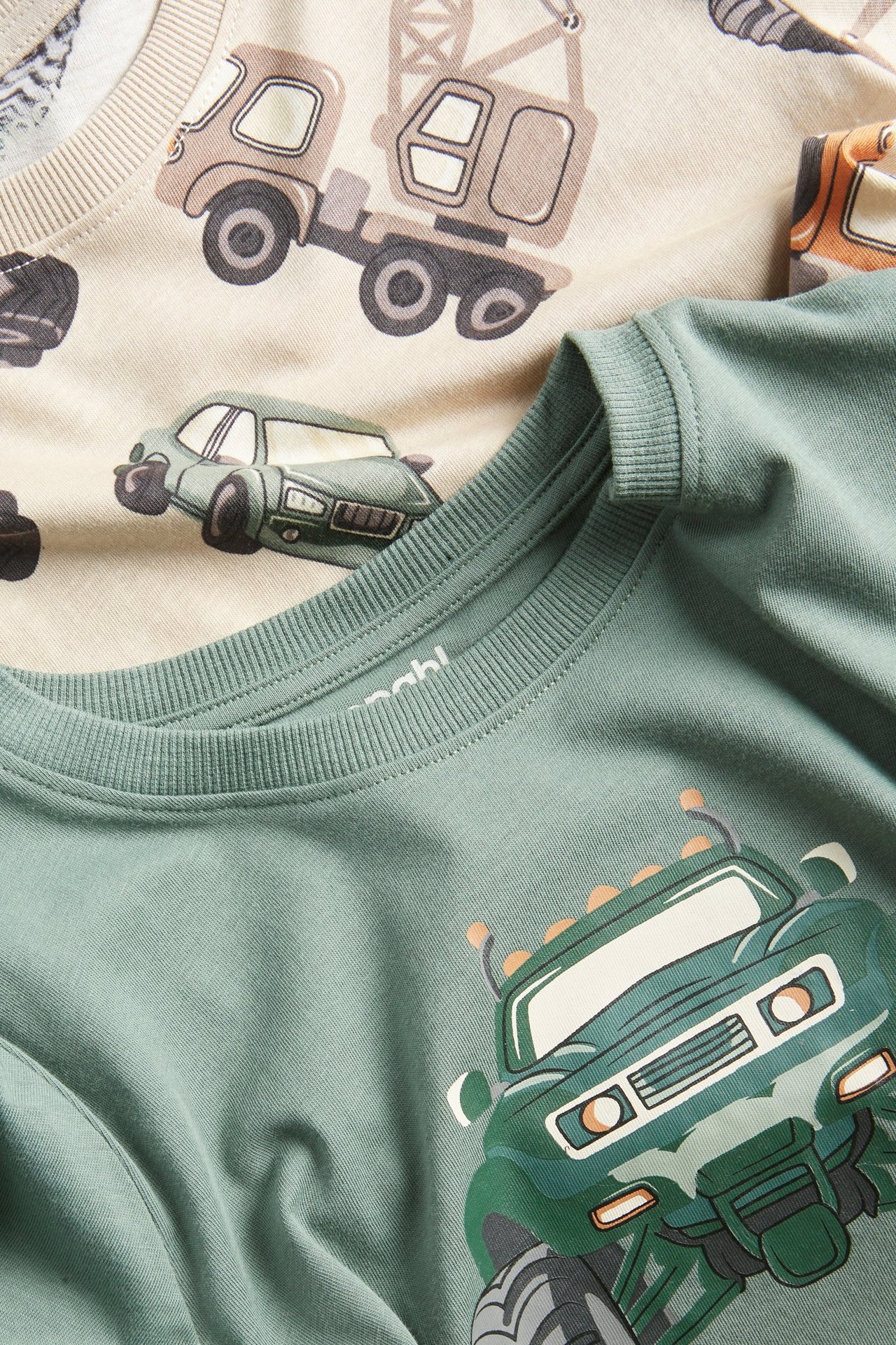 Zbliżenie: Dziecięca ciemnozielona bawełniana koszulka z długim rękawem z nadrukiem monster trucka. Beżowa koszulka z autami.