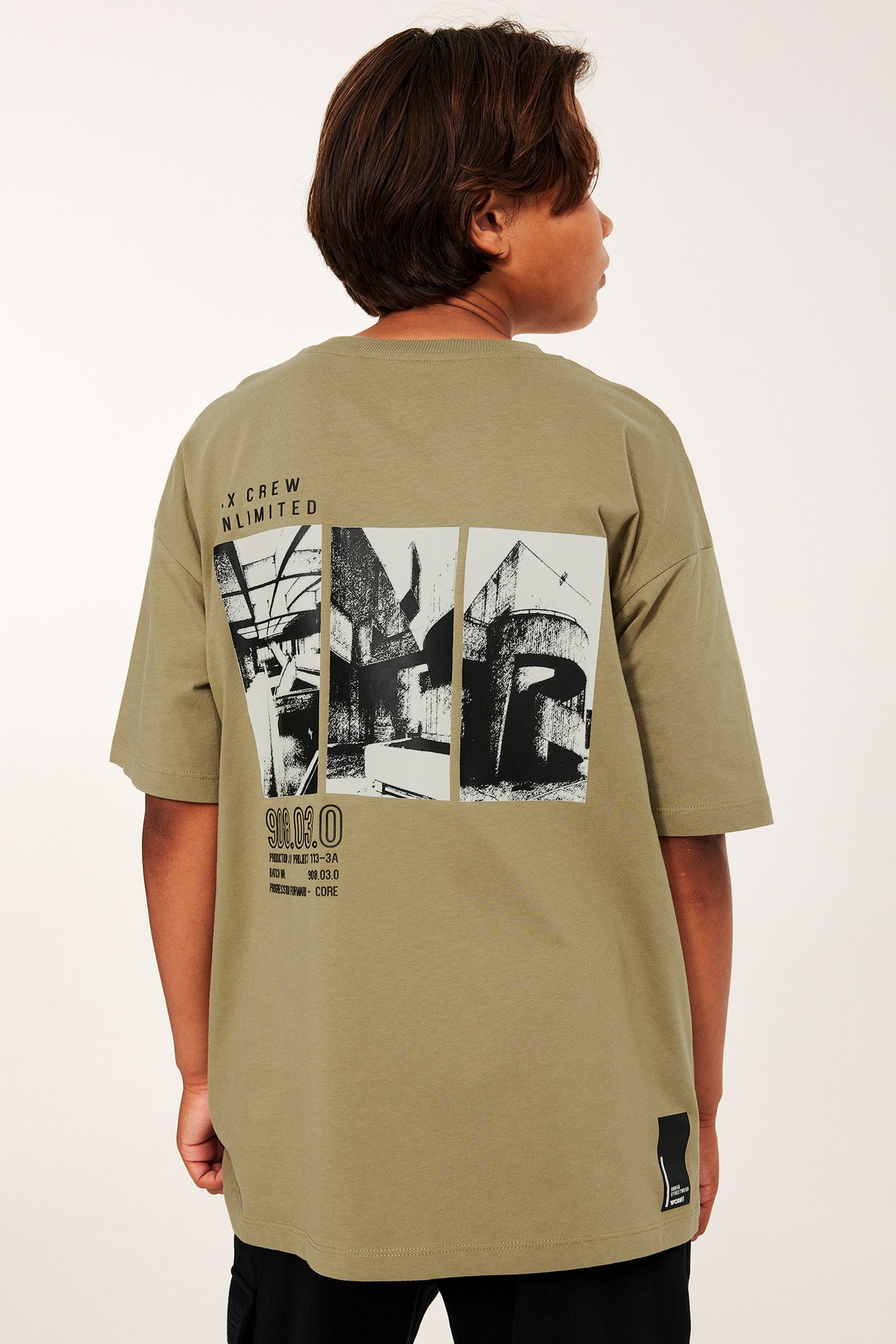 Bakifrån: ett barn i en khaki-brun bomulls-T-shirt med stort grafiskt tryck.