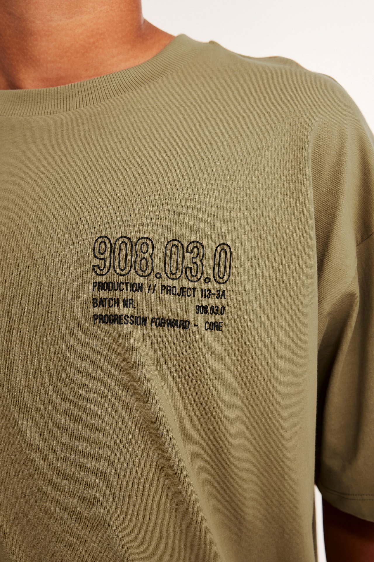 Närbild framifrån på en man i khakibrun bomulls-T-shirt med svart texttryck.
