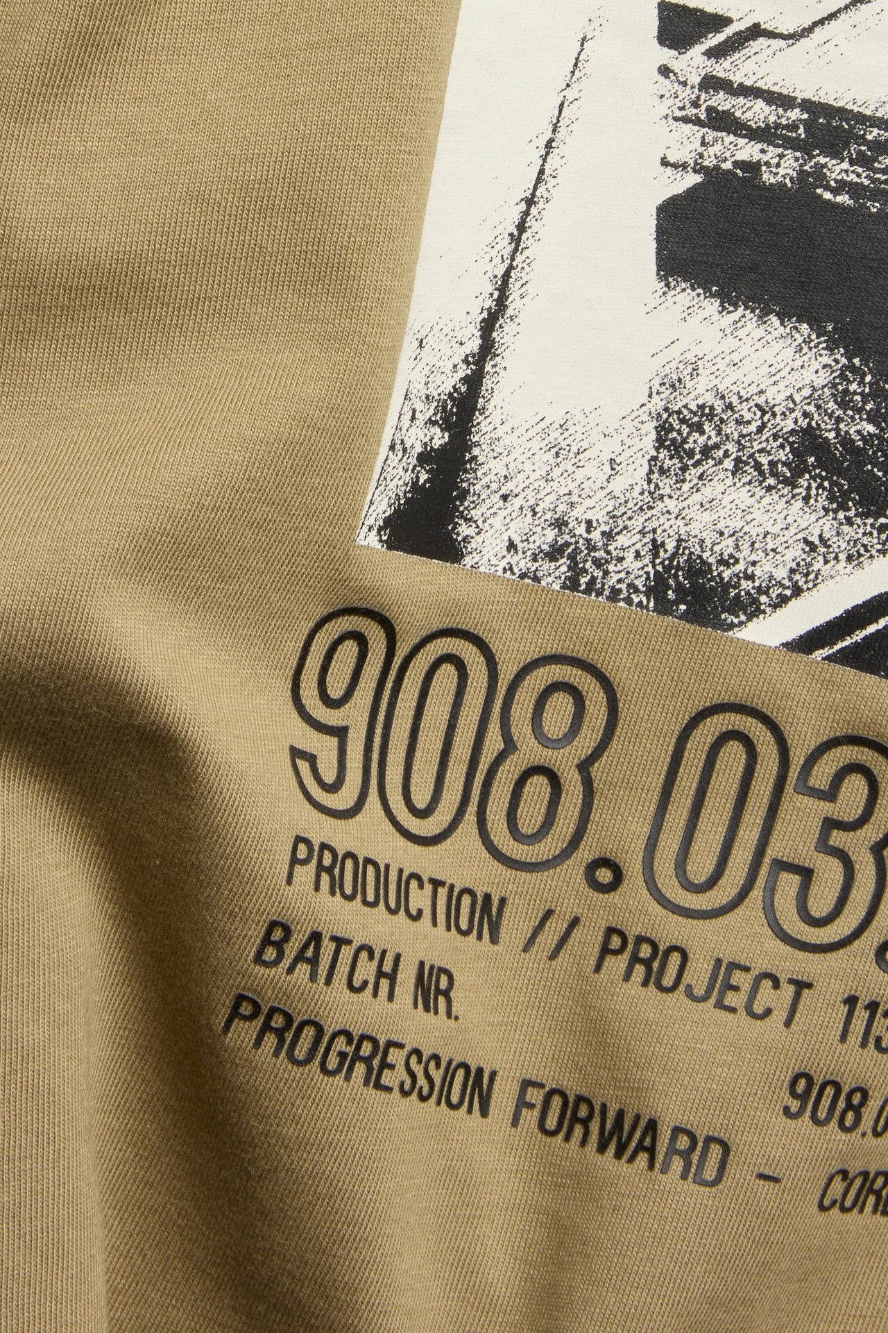 Zbliżenie na brązowy bawełniany T-shirt z czarno-białym nadrukiem graficznym i czarnym tekstem.