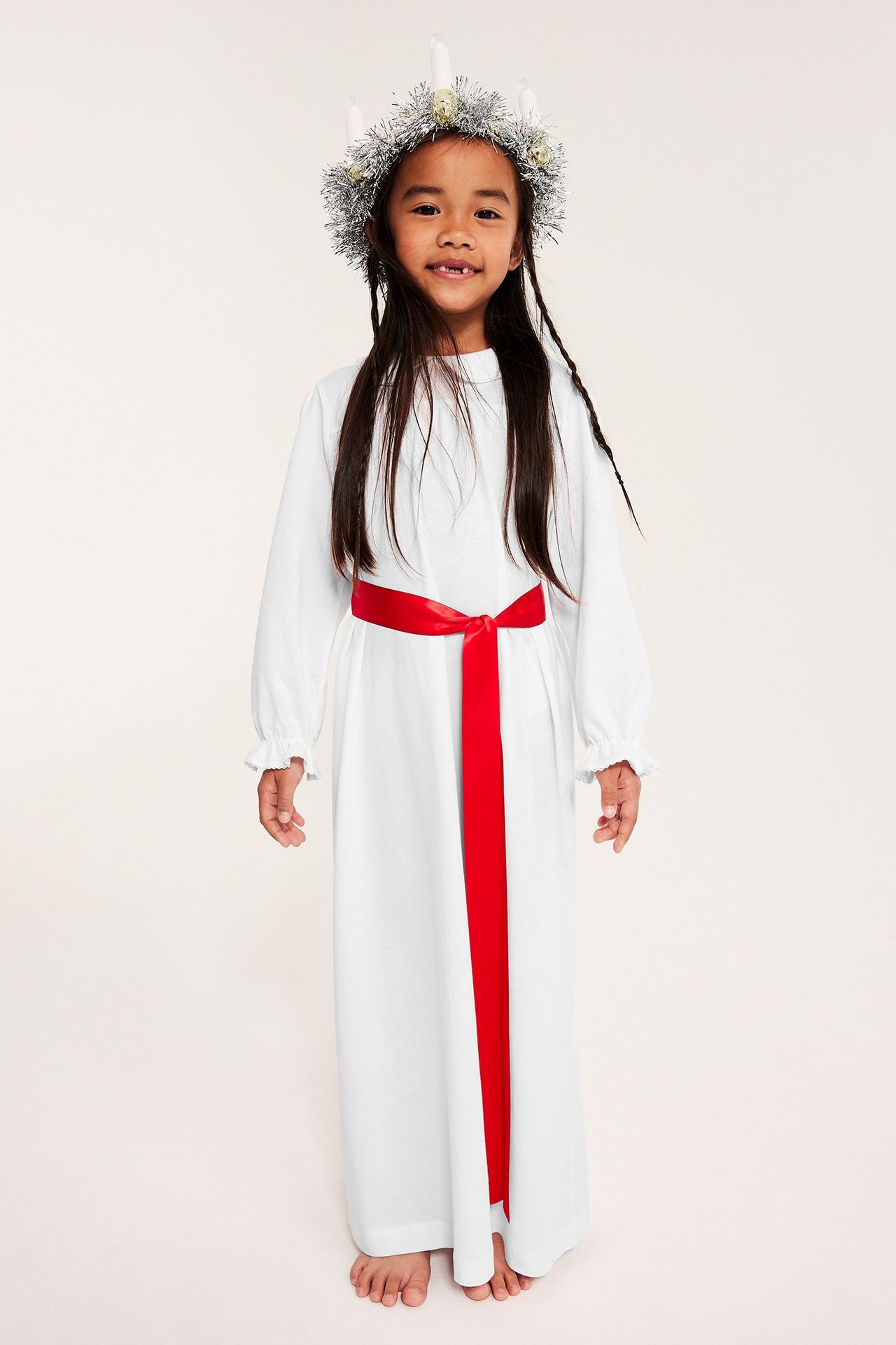 Jente i hvitt Lucia-nattlinne i jersey med rødt satengbånd og krage med picot-søm.