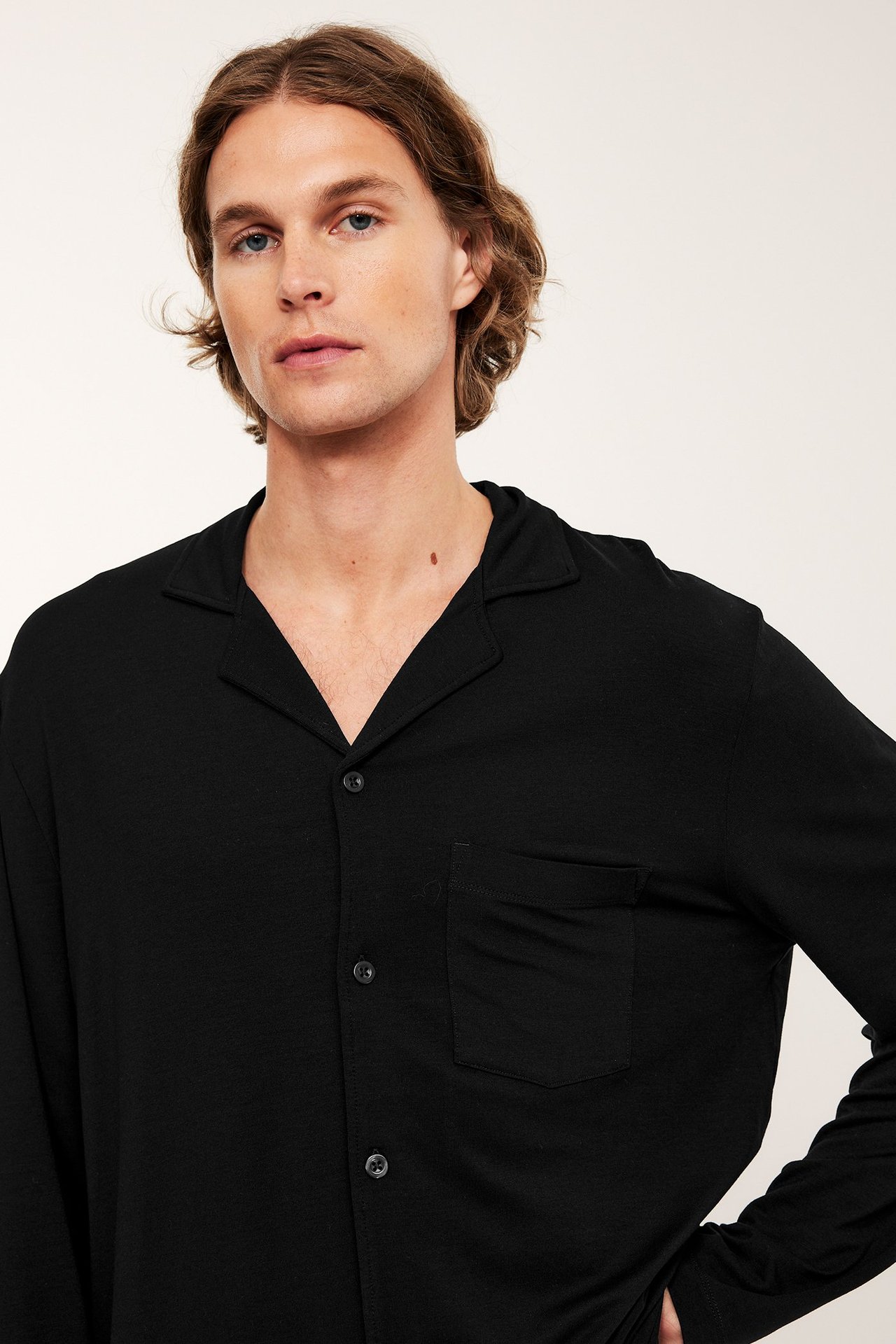 Edestä lähikuva miehestä yllään musta pitkähihainen pyjamapaita kauluksella ja rintataskulla.