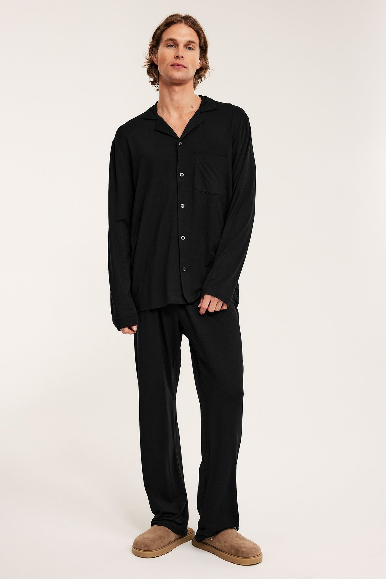 Edestä: mies mustassa pitkähihaisessa pyjamasettissä napeilla ja ruskeilla tohveleilla.