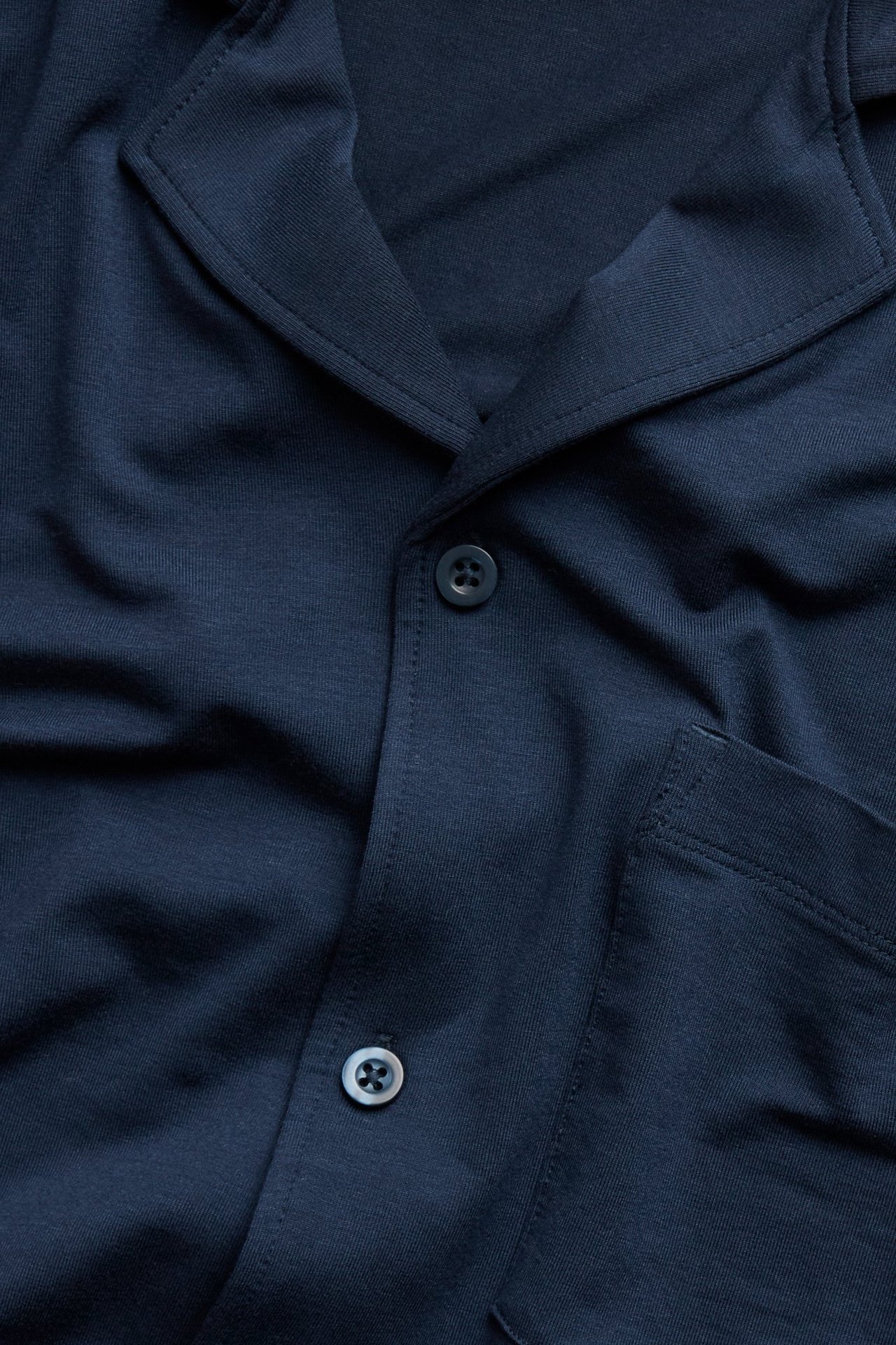 Zbliżenie przód: ciemnoniebieska gładka góra od piżamy z kołnierzem, guzikami i kieszenią na piersi.