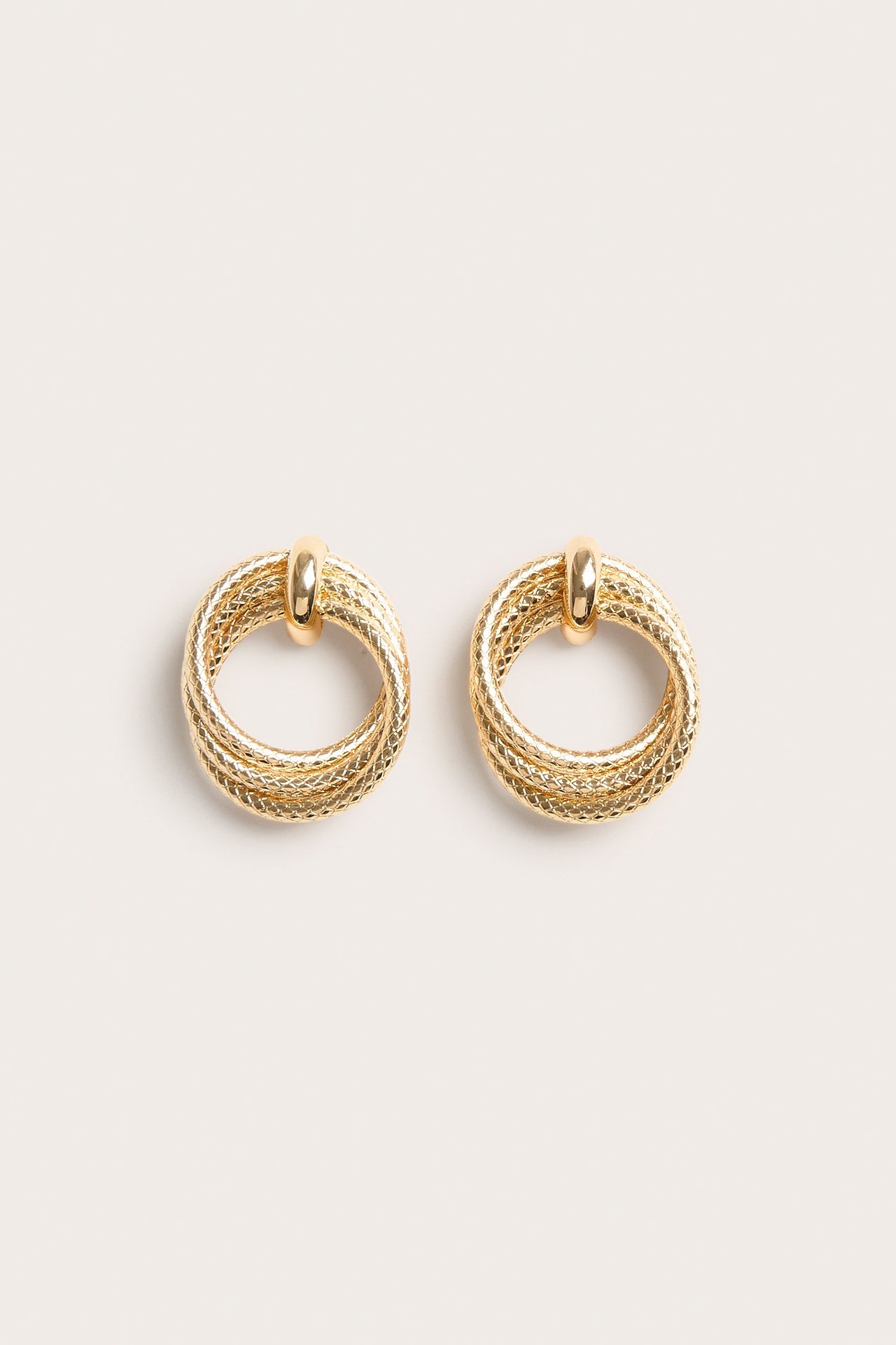 Zbliżenie z przodu na parę złotych metalowych kolczyków z wieloma splecionymi teksturowanymi pierścieniami.