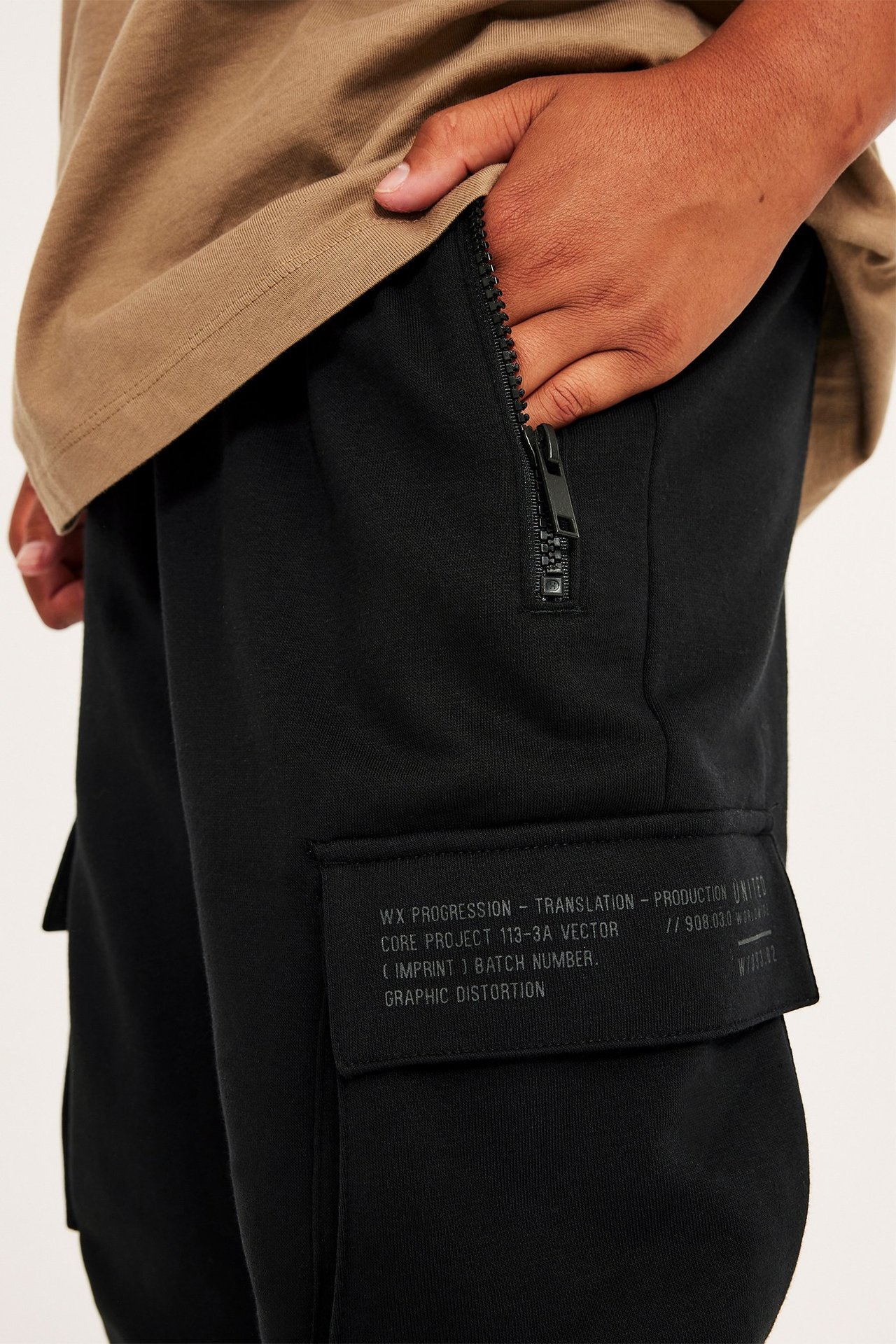 Zbliżenie na czarne dresowe spodnie dziecięce z kieszeniami na zamek i nadrukowanymi kieszeniami cargo, z brązowym T-shirtem.