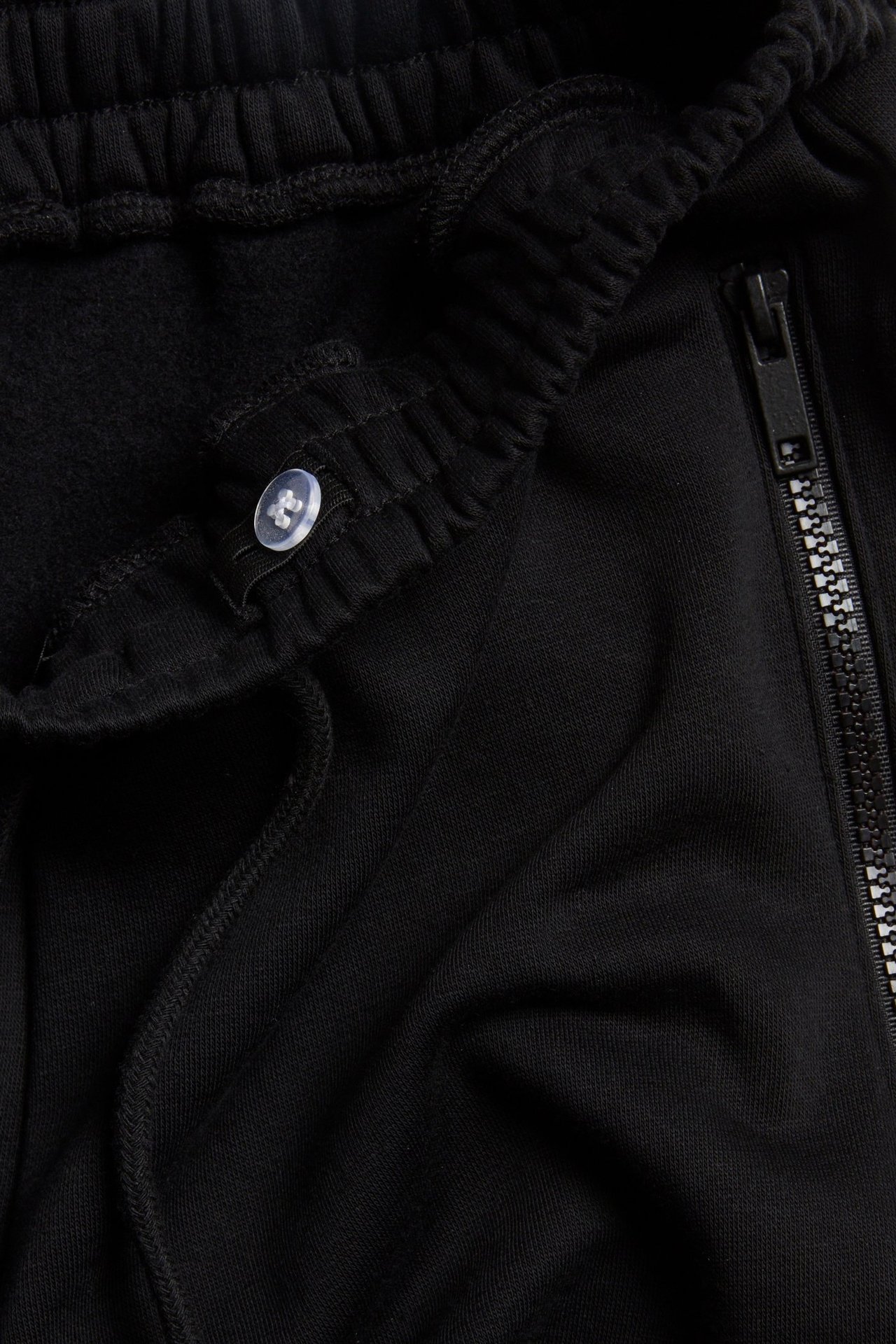 Zbliżenie czarnych spodni dresowych z elastycznym pasem ze sznurkiem, przezroczystym guzikiem i kieszenią na zamek.