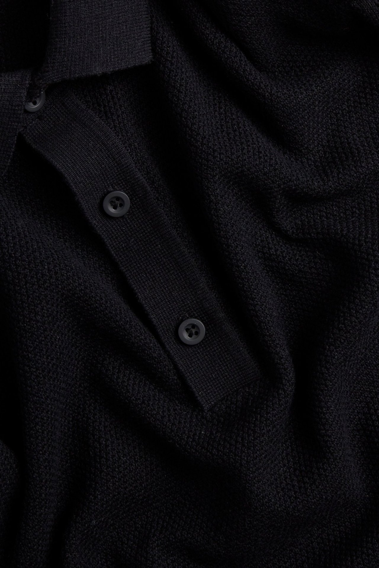 Zbliżenie czarnego, dzianinowego swetra męskiego ze wzorem strukturalnym, kołnierzem i guzikami z przodu.