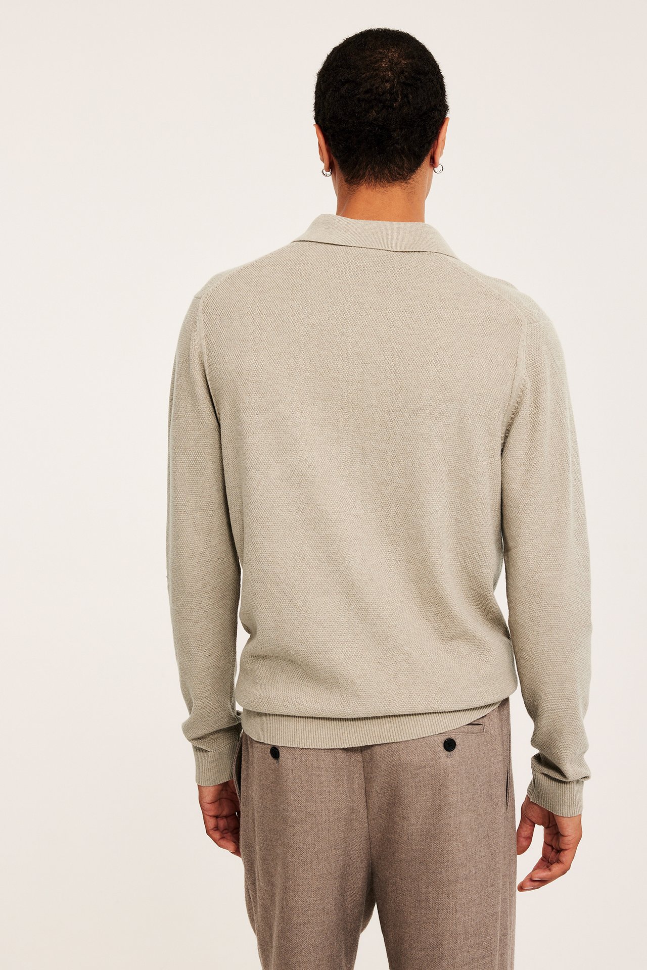 Miehen takakuva: beige melange -värinen struktuurineulottu polopaita ja ruskeat melange -housut.